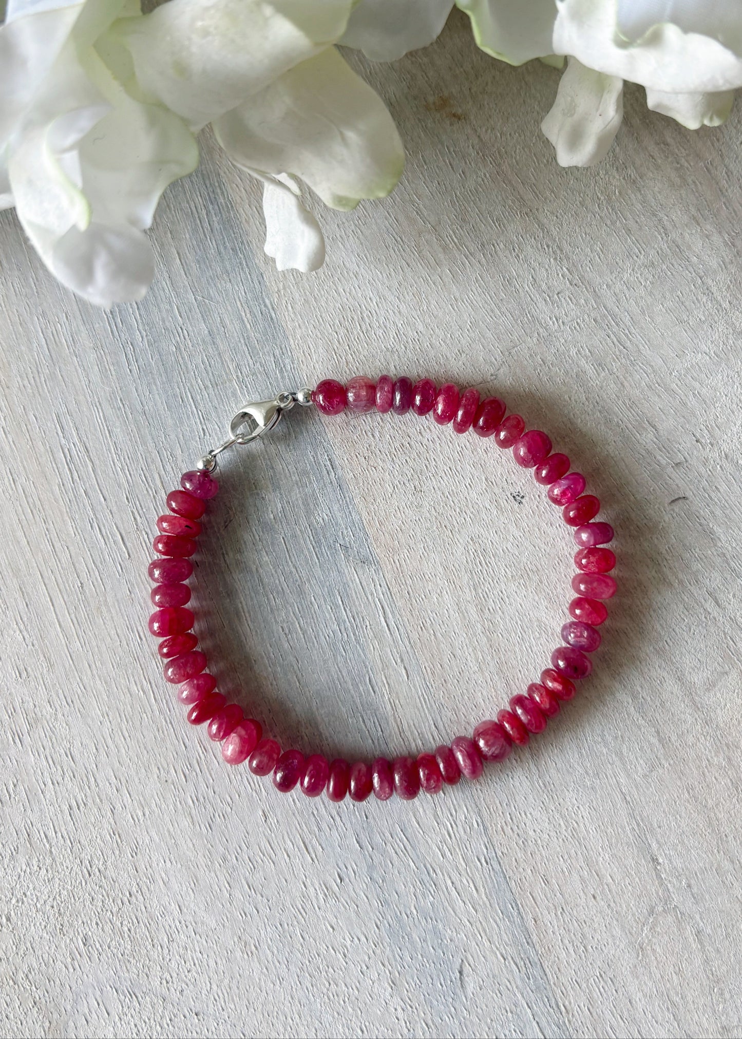Red beaded bracelet on a light wooden surface with white flowers in the background