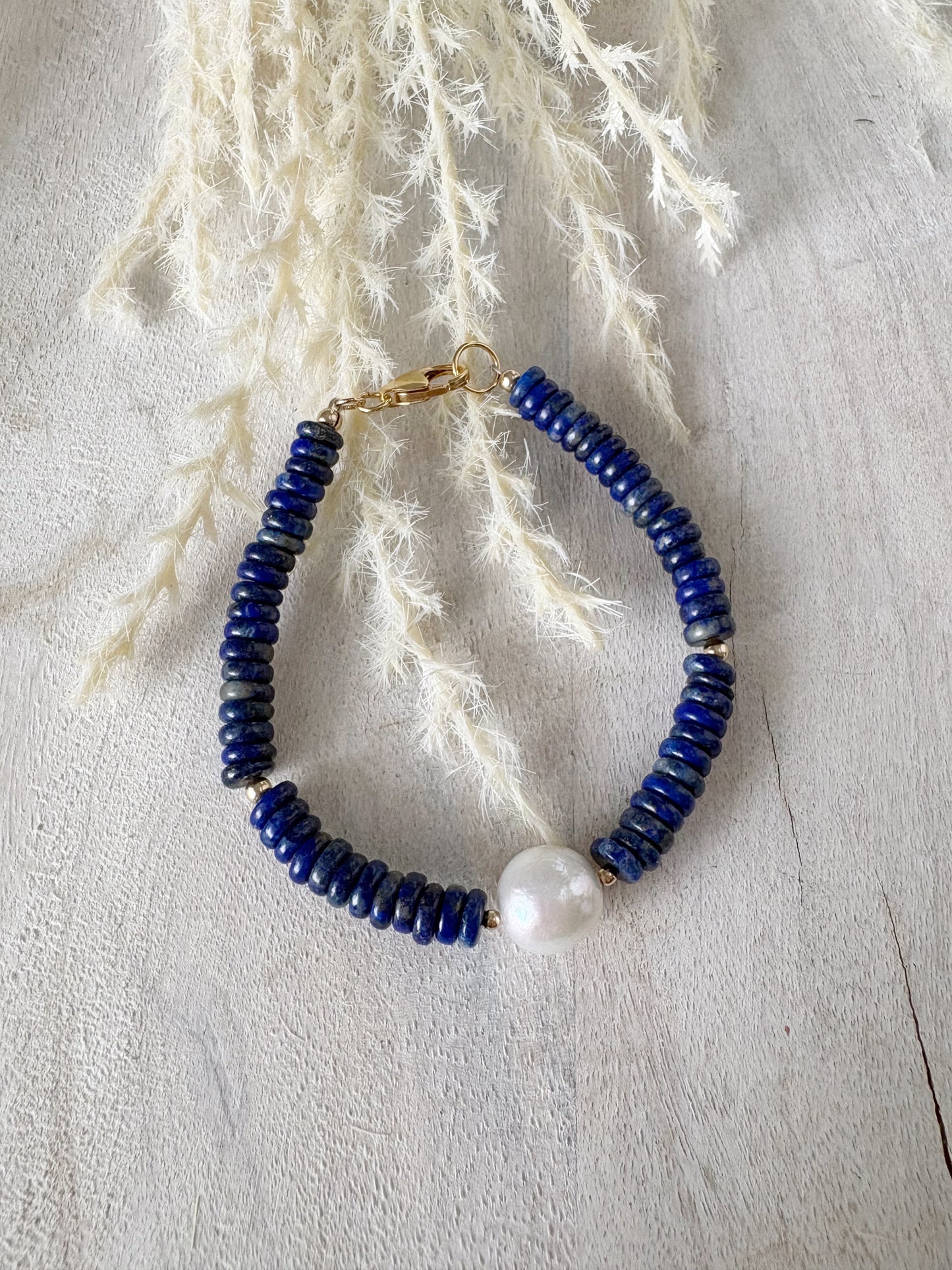 Lapis and Pearl Bracelet with blue lapis beads and a single white pearl on a light wooden surface