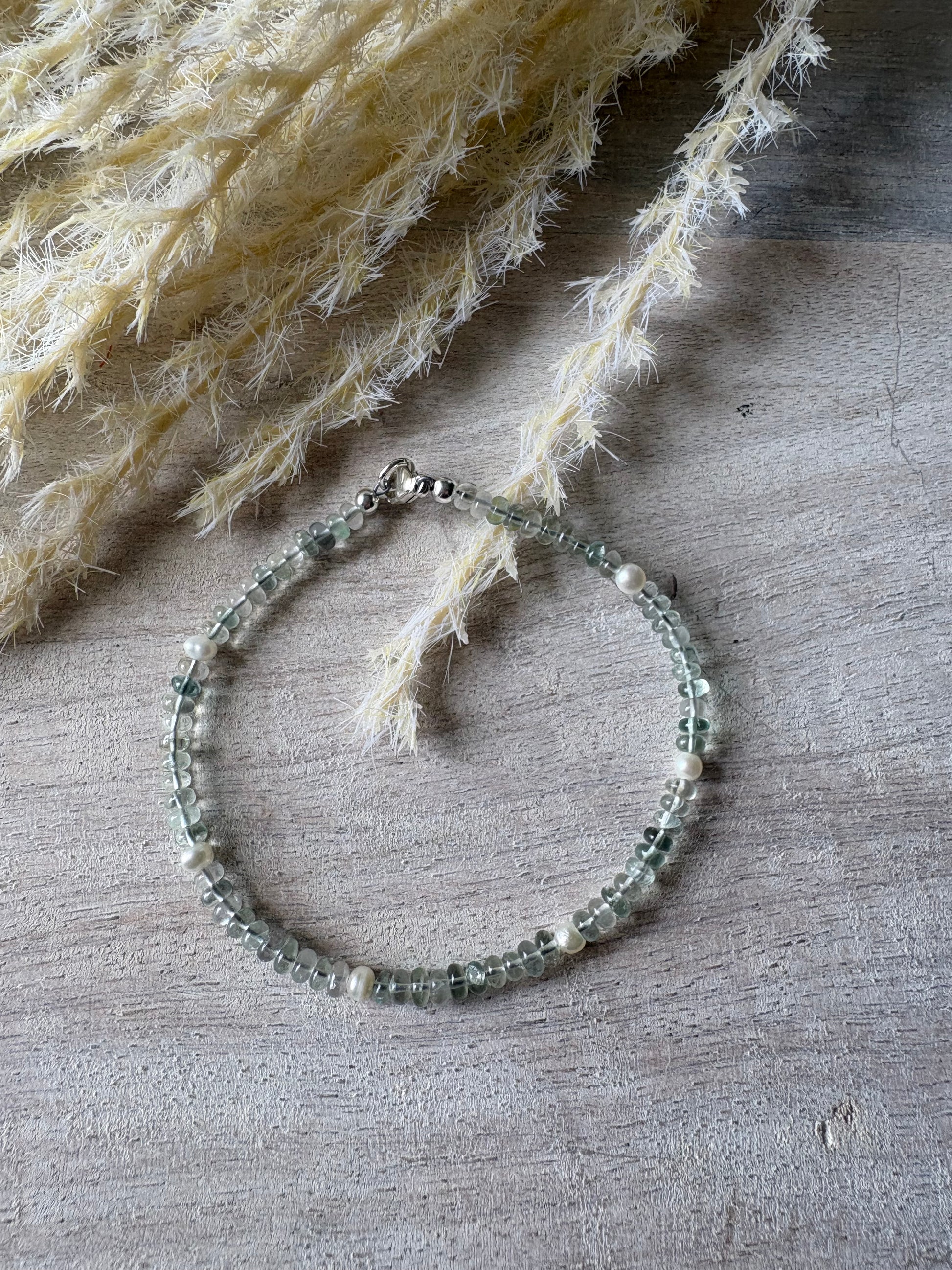 Fluorite and Pearl Bracelet with light green fluorite beads and white pearls on a wooden surface