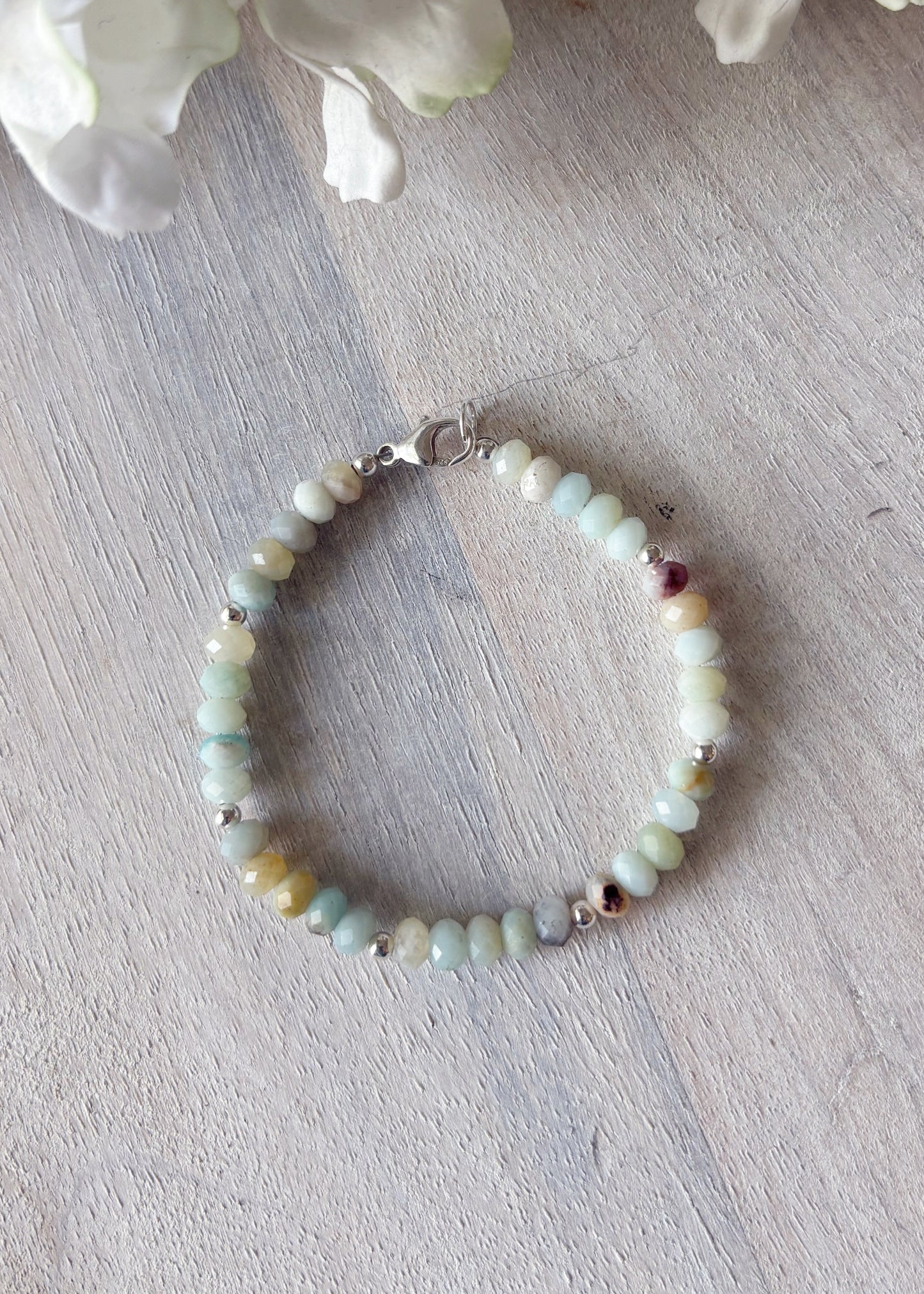 Beaded bracelet on a light wooden surface with white flowers in the background