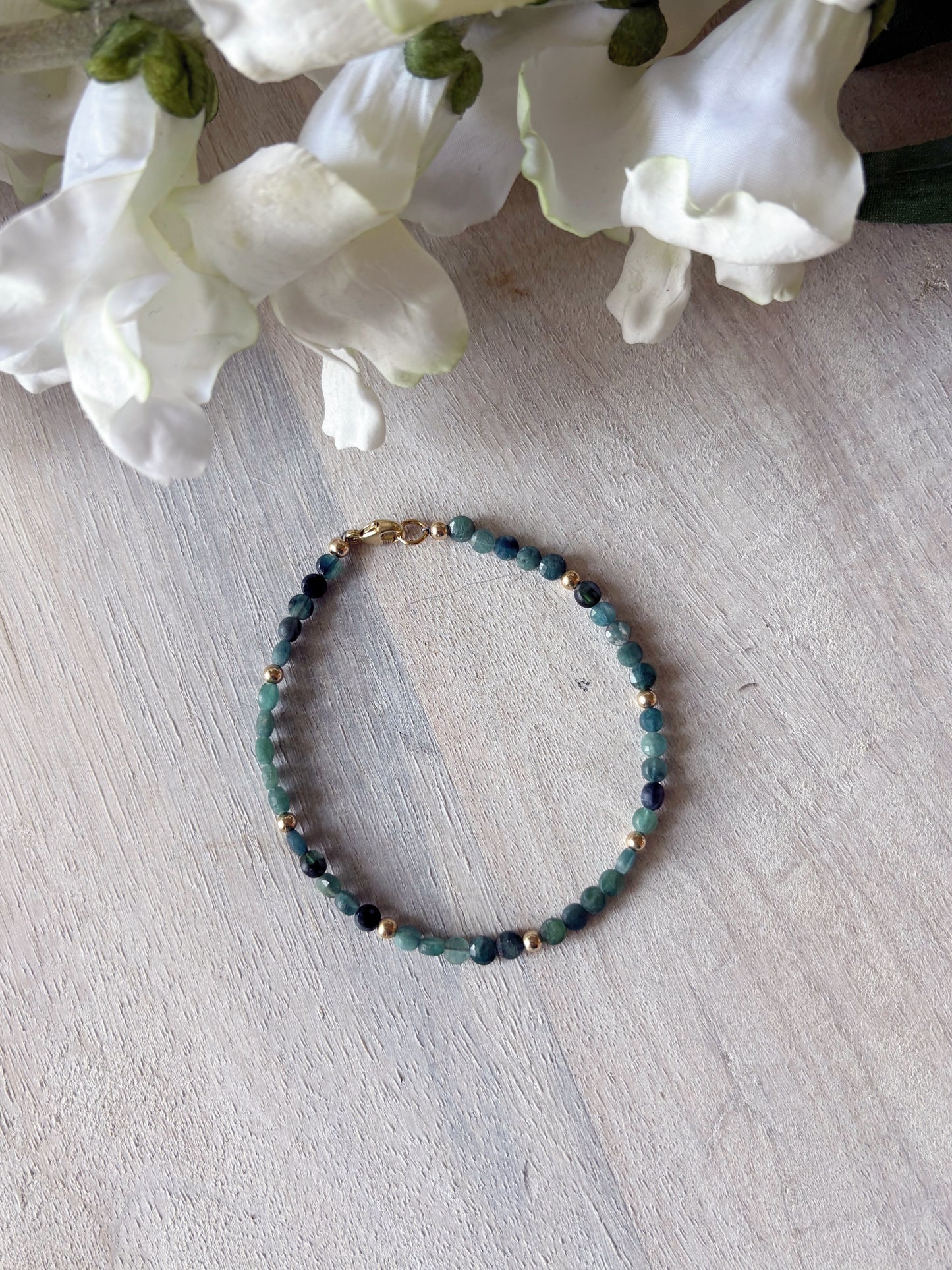 Beaded bracelet on a light wooden surface with white flowers in the background