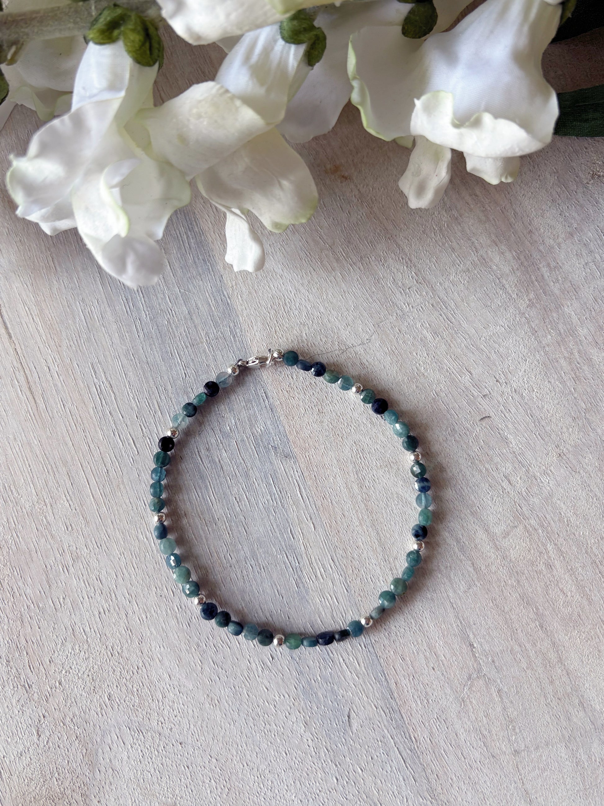 Beaded bracelet on a light wooden surface with white flowers in the background