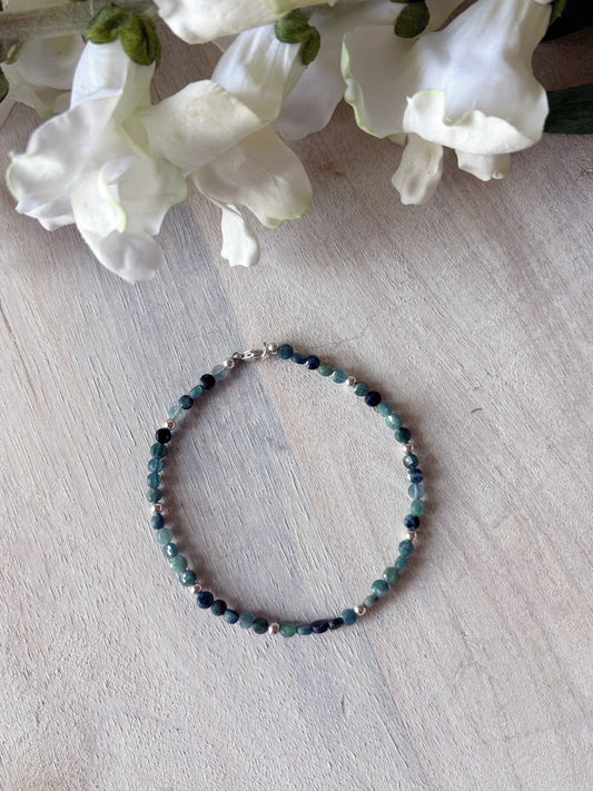 Beaded bracelet on a light wooden surface with white flowers in the background