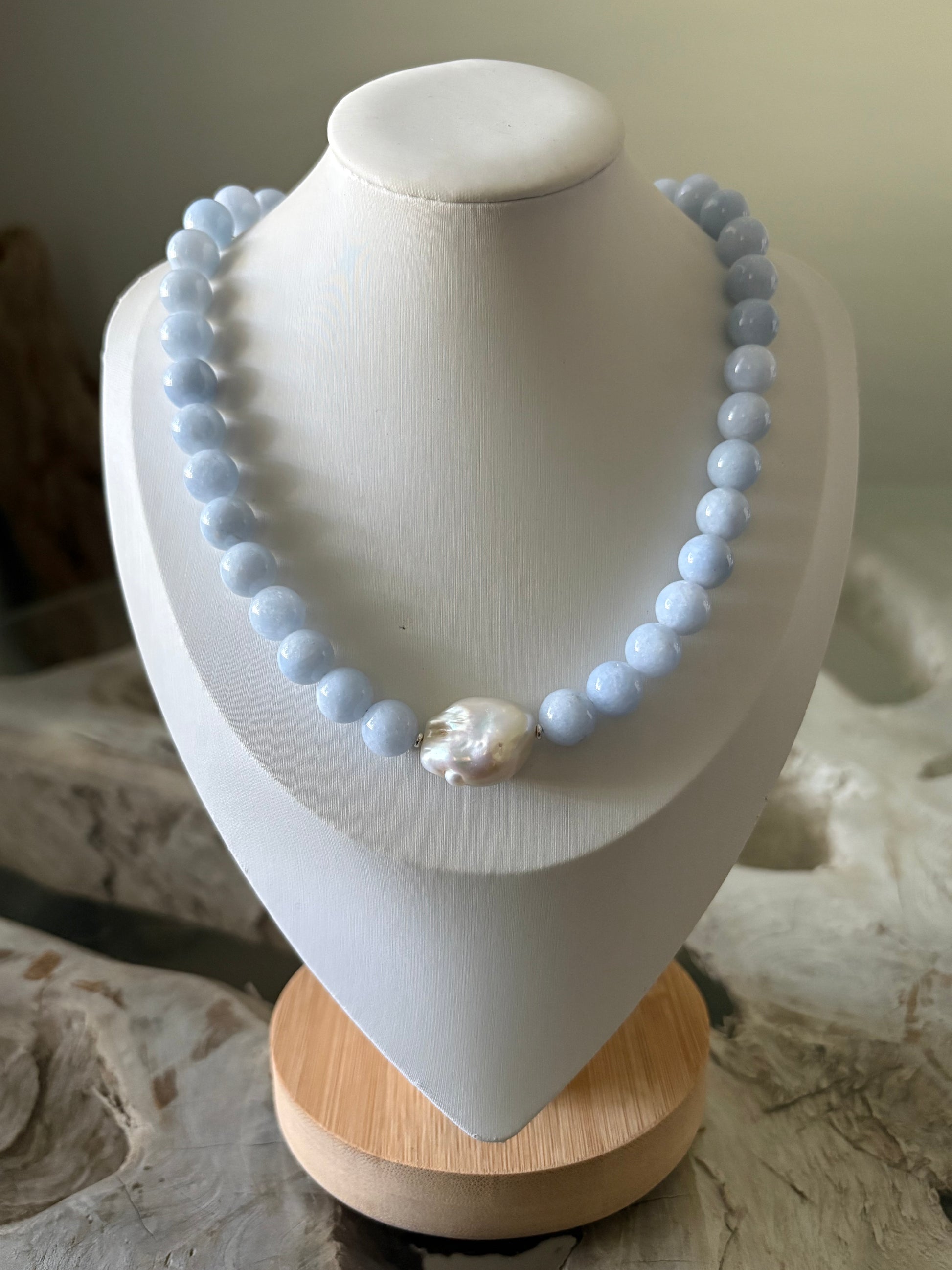 A light blue beaded necklace with a single large white pearl accent, displayed on a white jewelry bust.