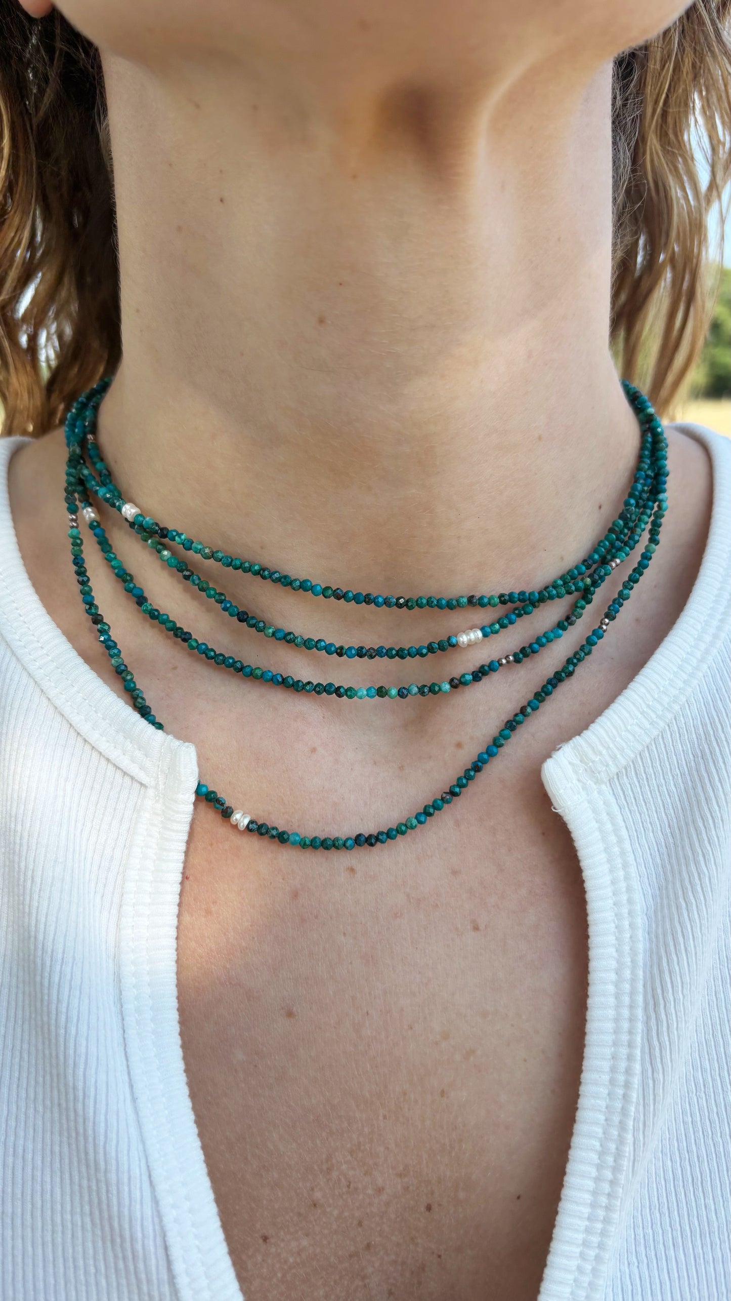 Long chrysocolla necklace with small turquoise beads and white pearl accents worn around the neck