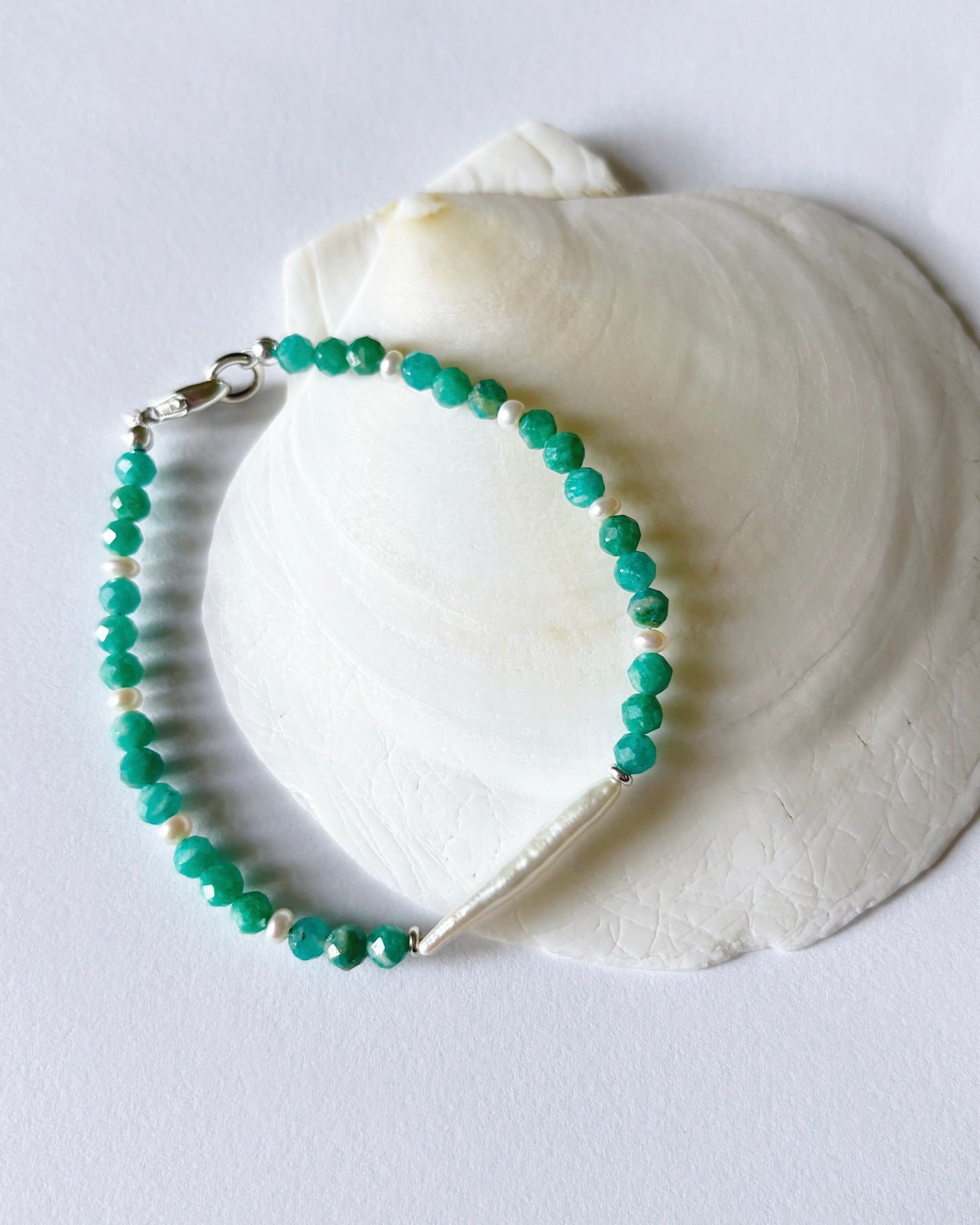 Green beaded bracelet on a white shell against a light gray background