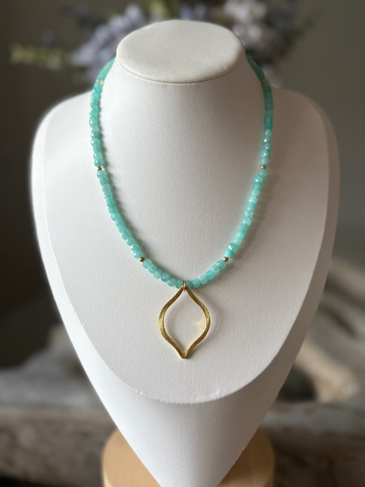 Turquoise beaded necklace with a gold pendant on a white mannequin bust.