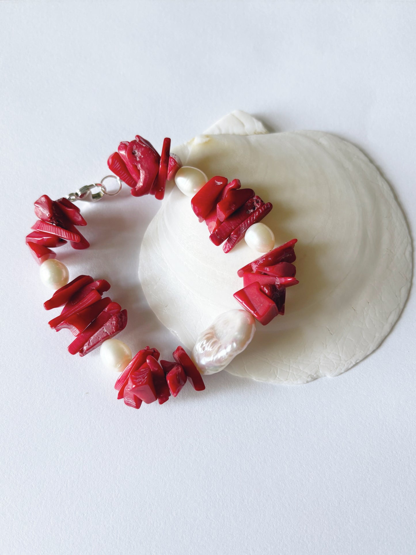 Bracelet with red coral-like beads and pearls on a white shell against a white background