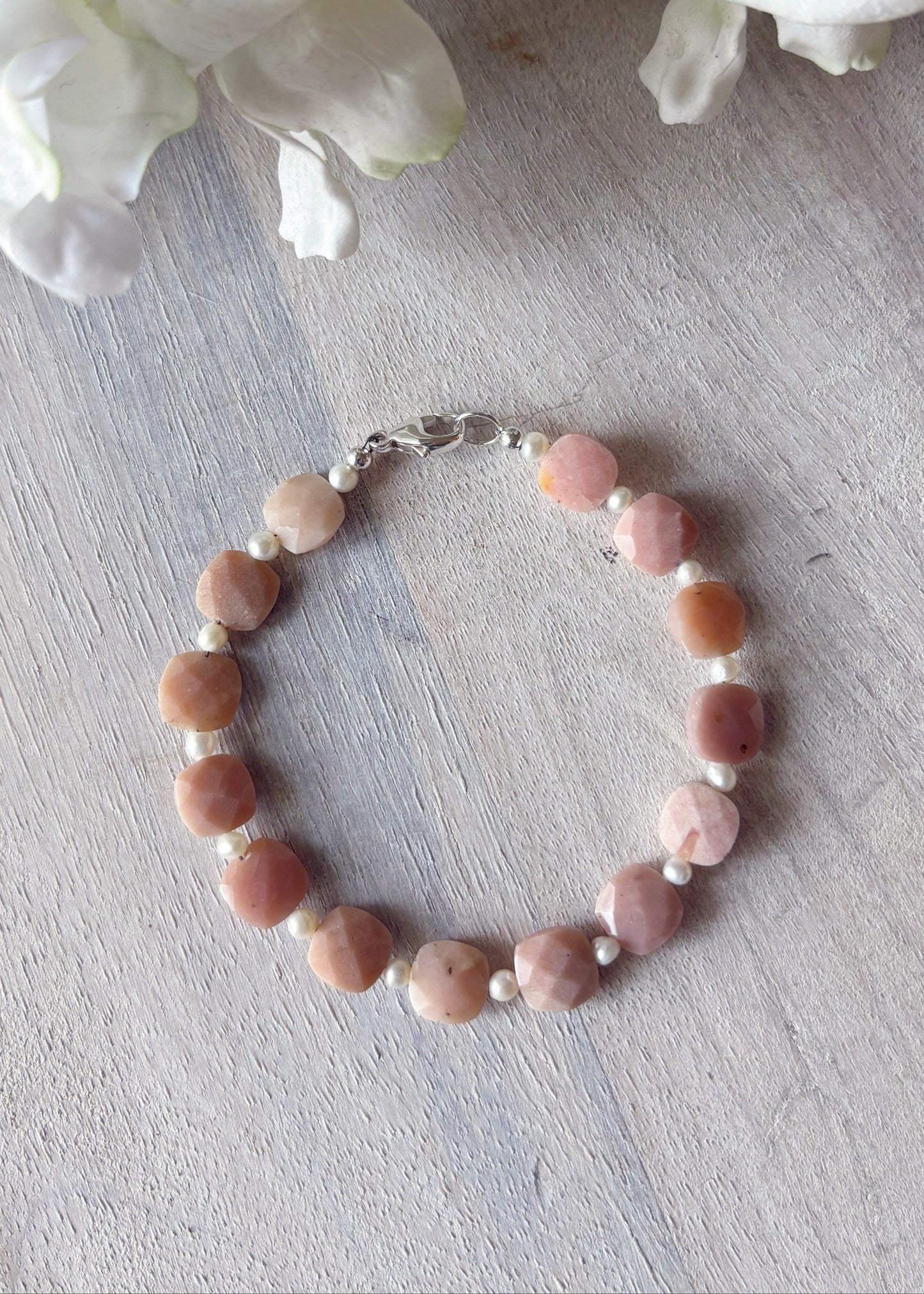 Bracelet with pink and white beads on a light wooden surface with flowers in the background