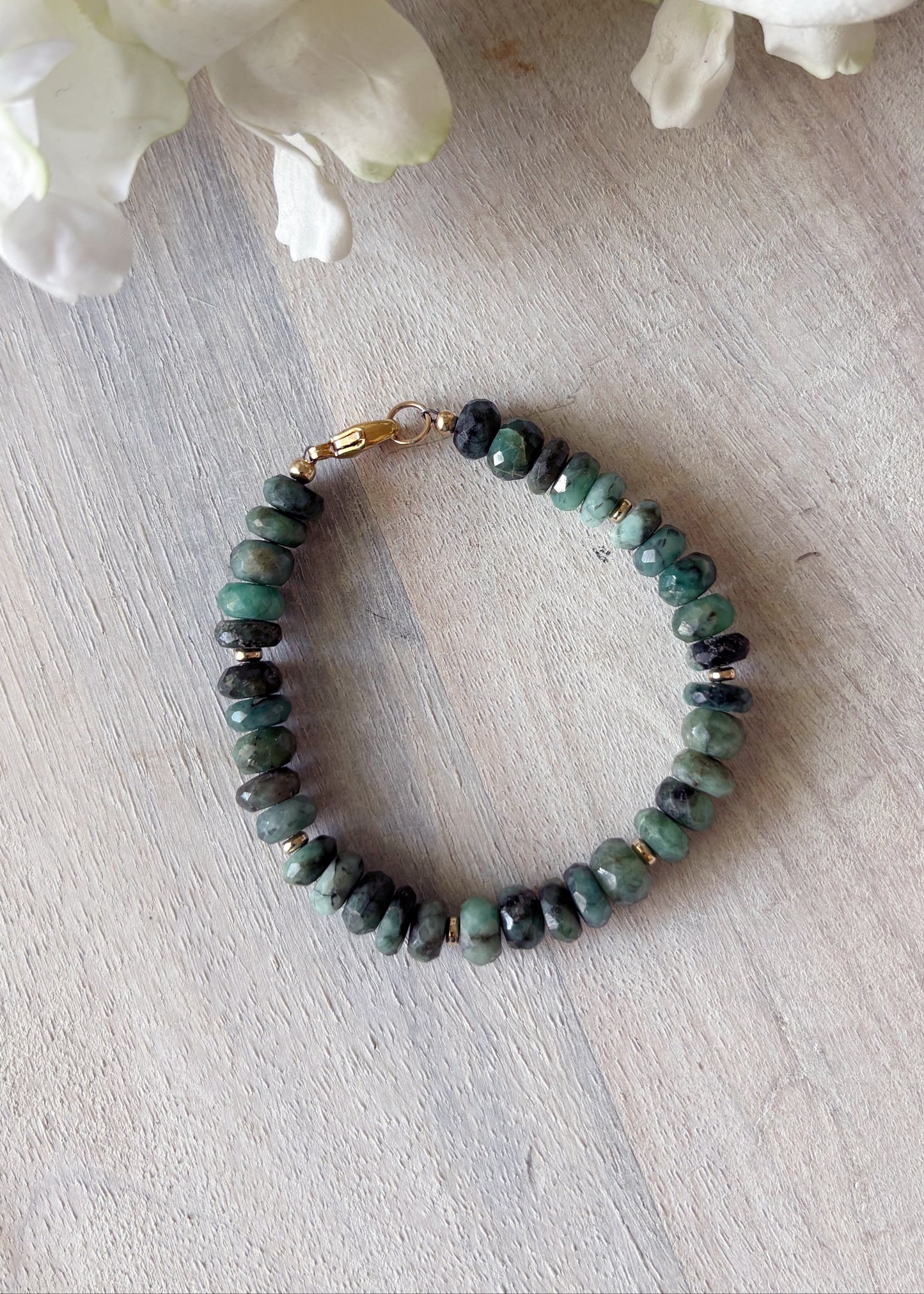 Green beaded bracelet on a light wooden surface with white flowers in the background