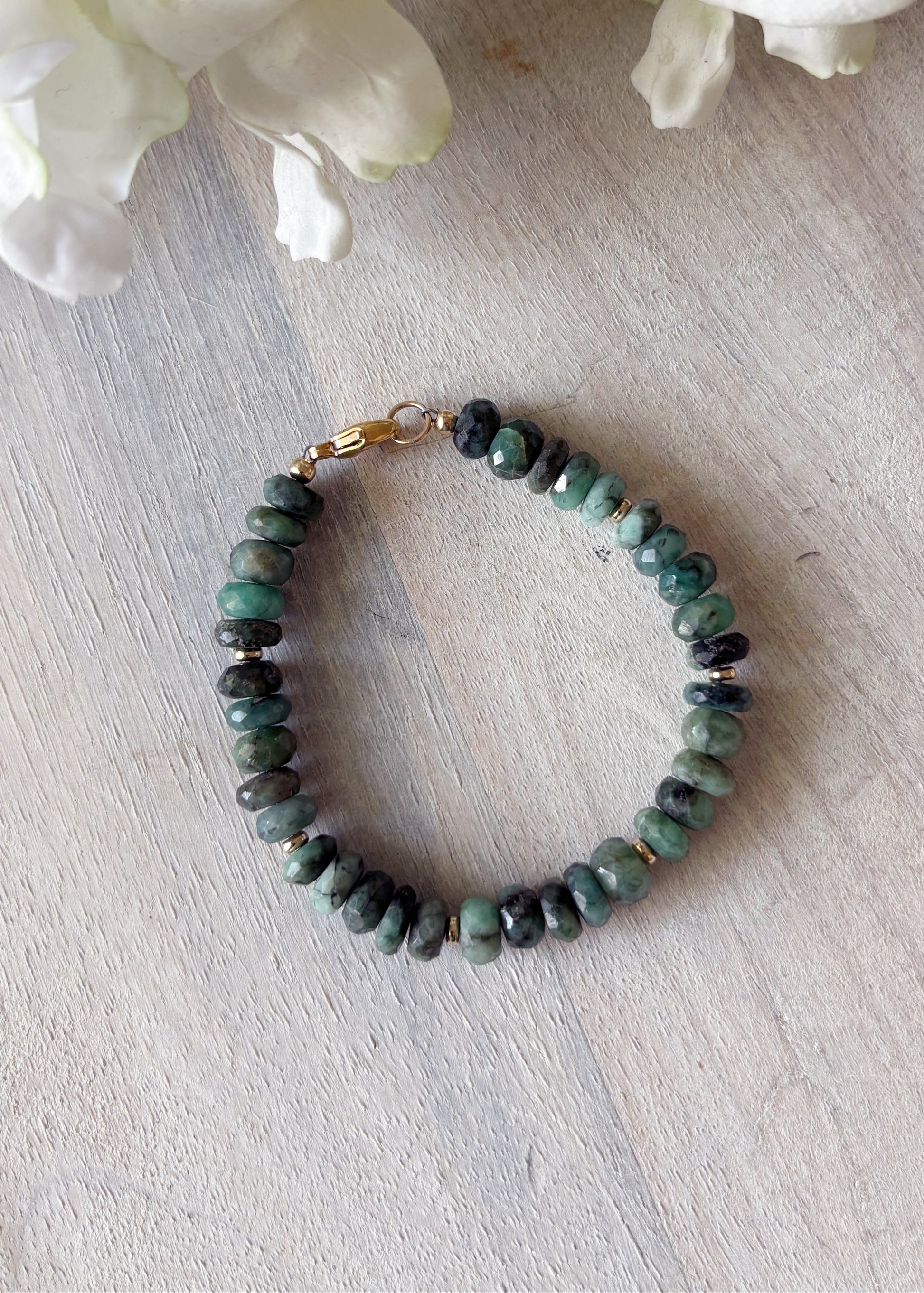 Green beaded bracelet on a light wooden surface with white flowers in the background