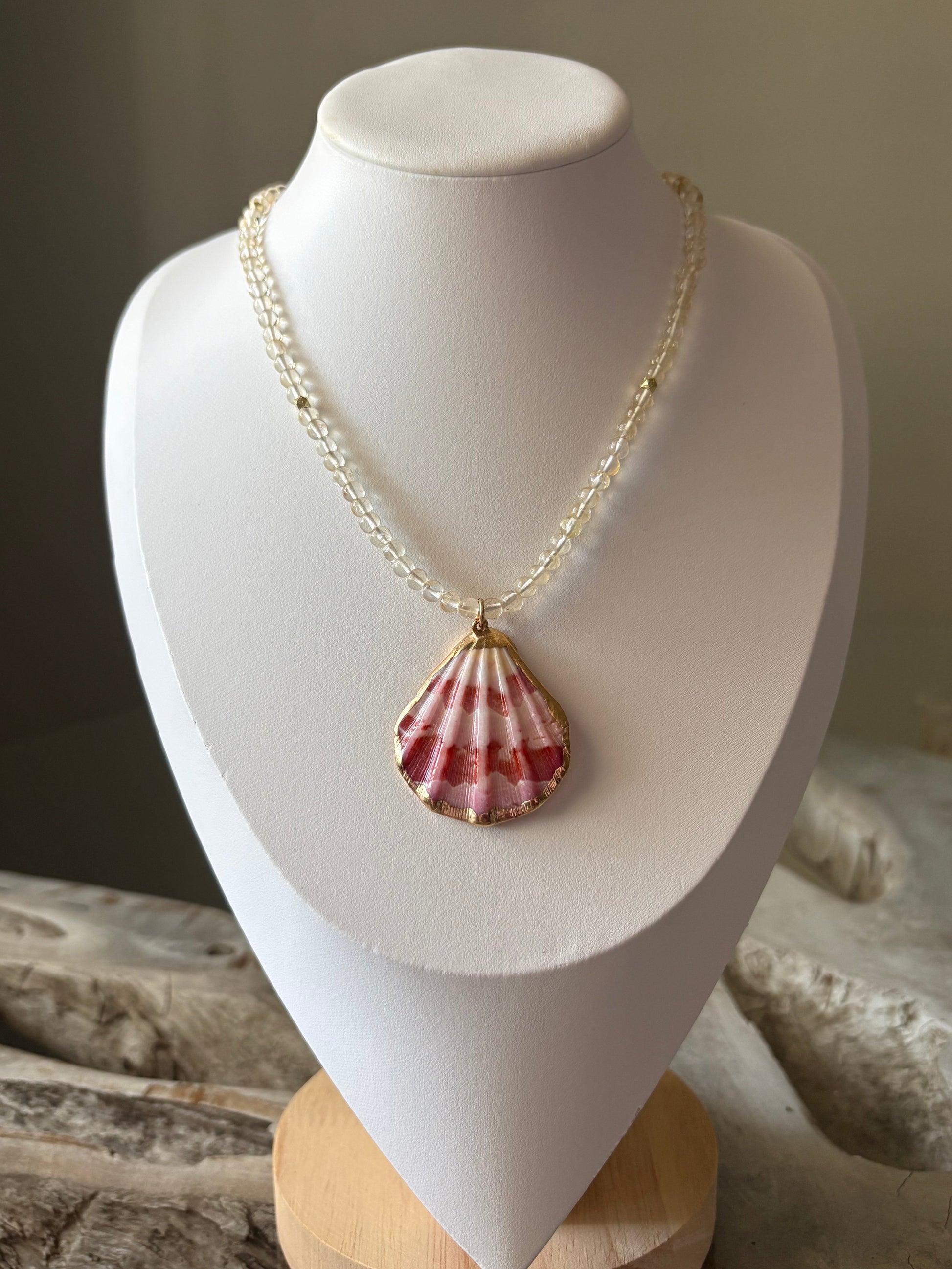 Necklace with a shell pendant on a mannequin bust against a neutral background