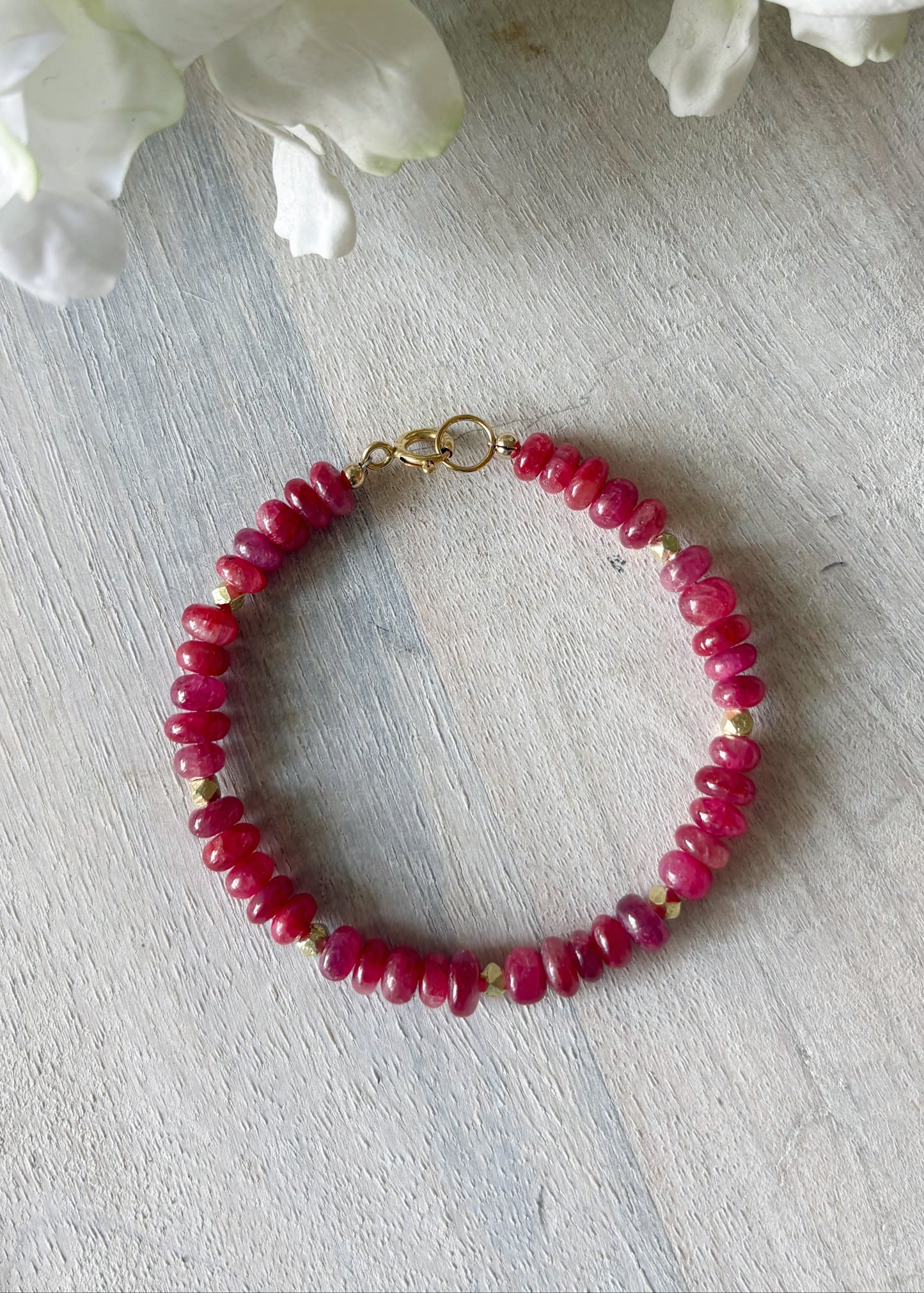 Bracelet with red beads on a light wooden surface with white flowers in the background