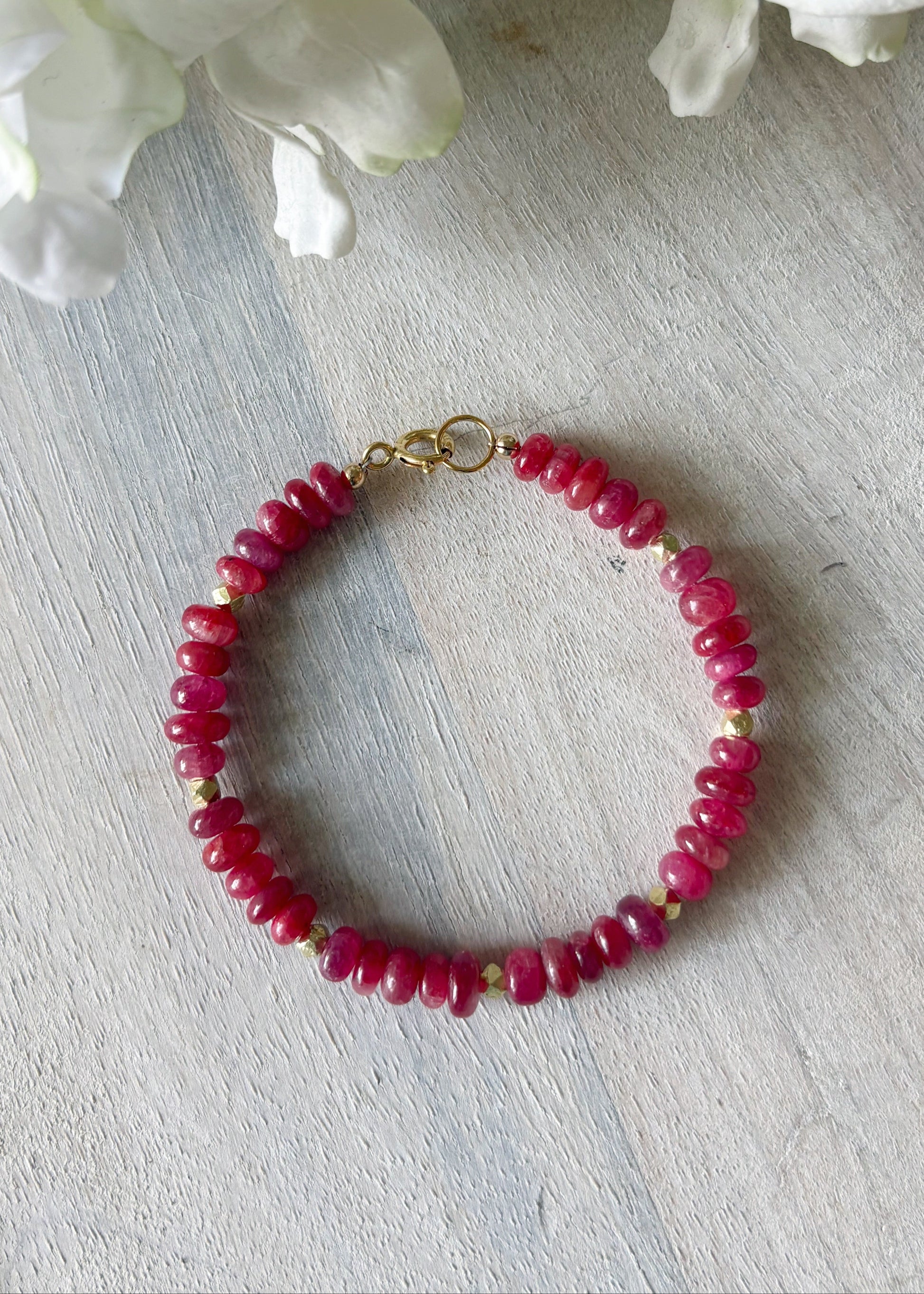 Bracelet with red beads on a light wooden surface with white flowers in the background