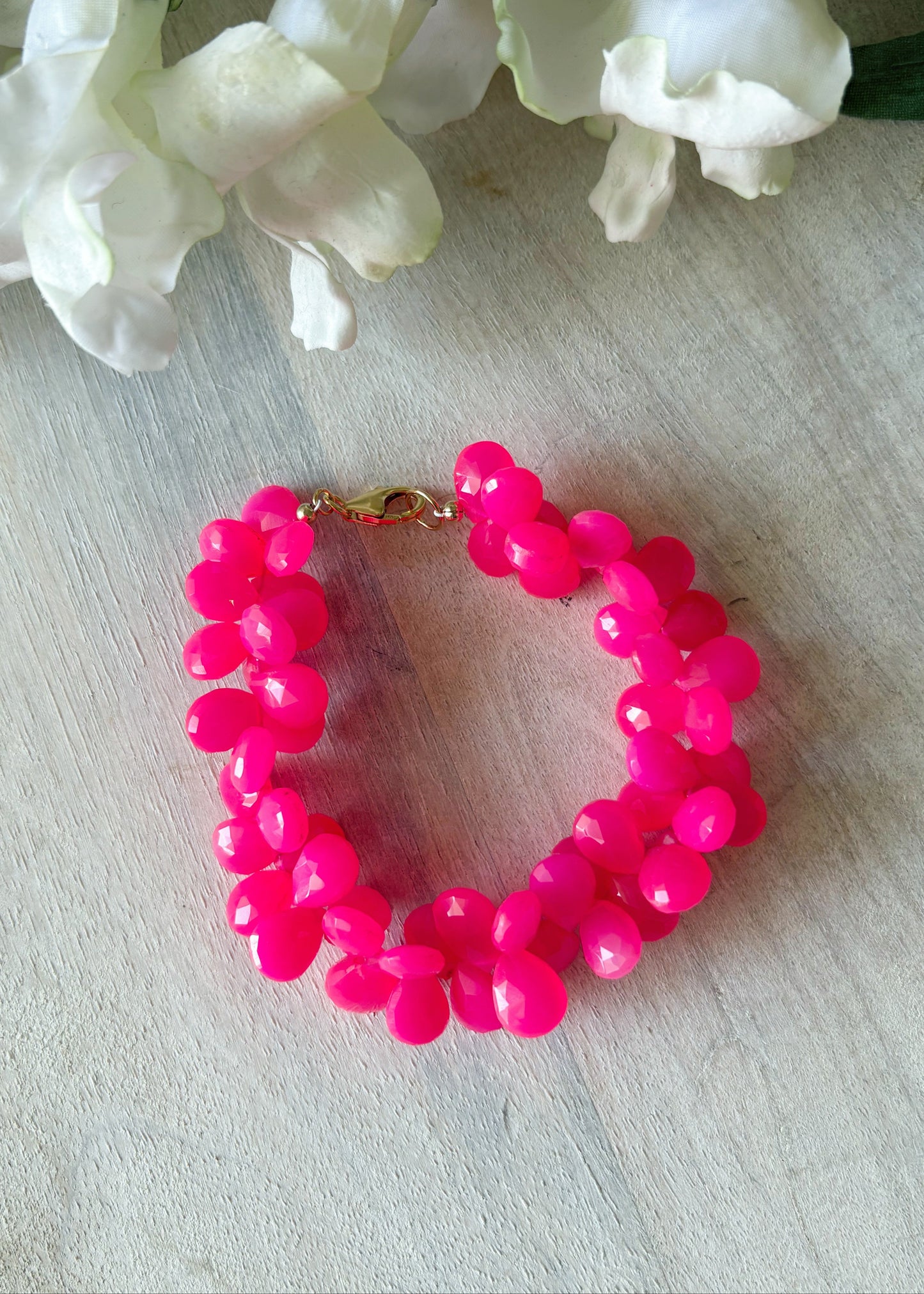 Hot pink beaded bracelet on a light wooden surface with white flowers in the background