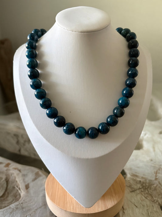 A beaded necklace made of dark blue polished round beads, displayed on a white jewelry bust with a light wood base.