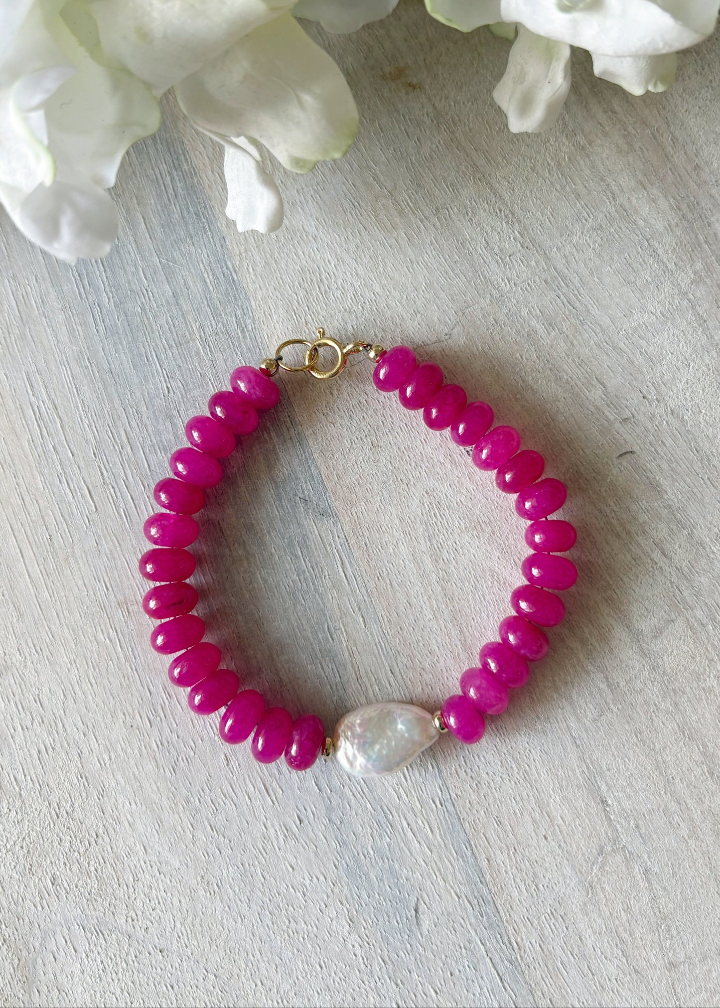 Pink beaded bracelet with a pearl on a light wooden surface with white flowers in the background