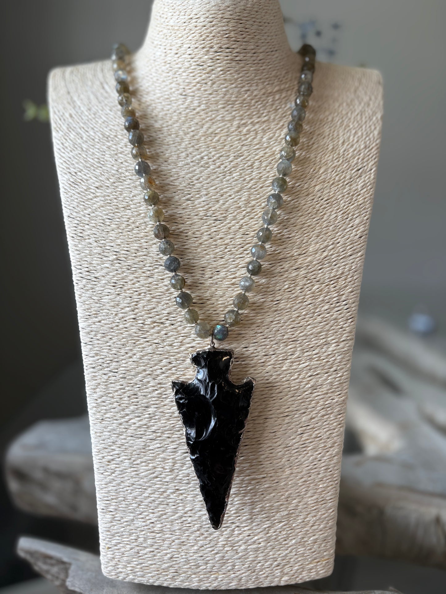 Necklace with a black arrowhead pendant on a beige stand.