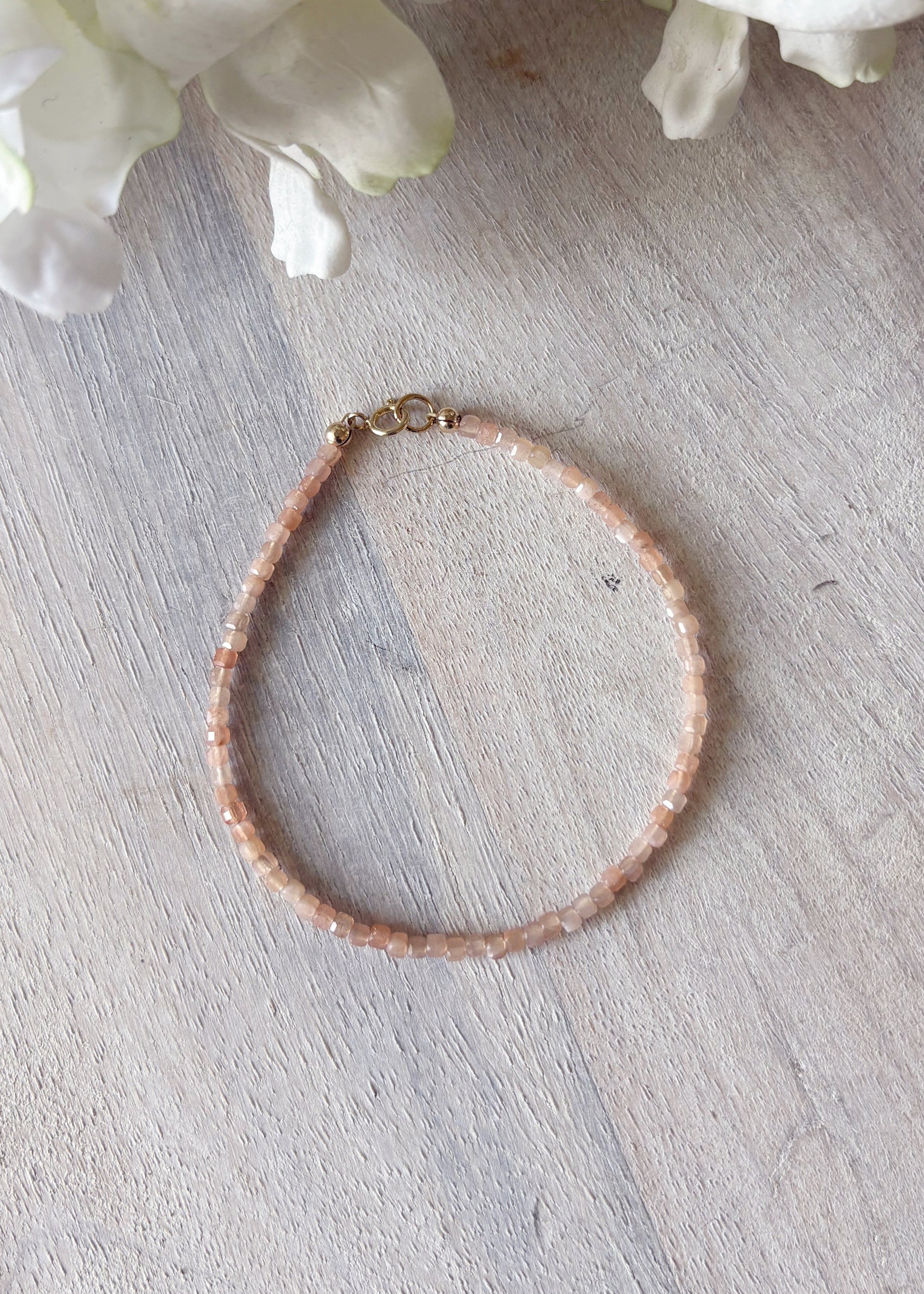 Peach moonstone  bracelet on a light wooden surface with white flowers in the background