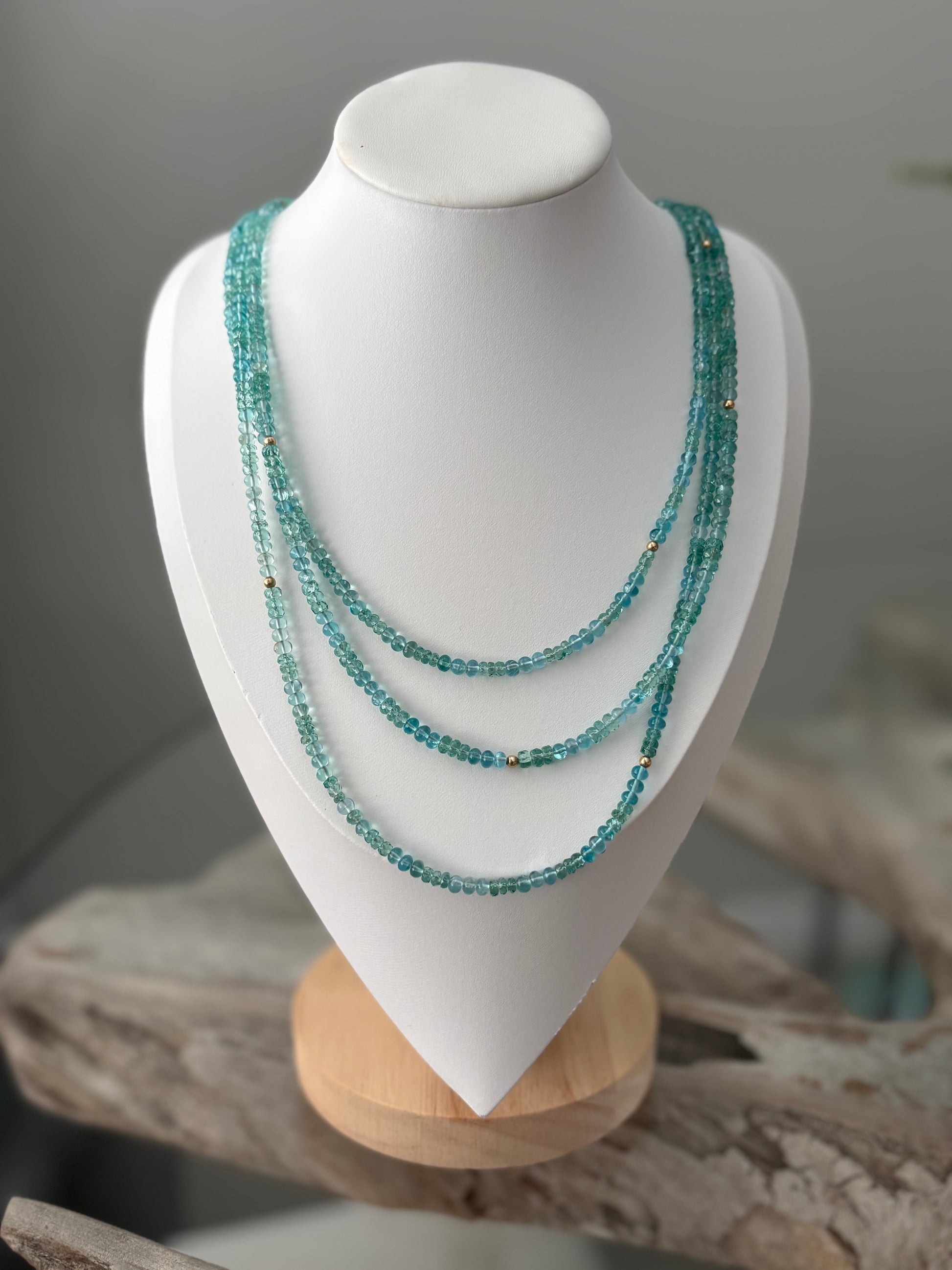 Multistrand turquoise beaded necklace on a white mannequin bust with a natural wood base.