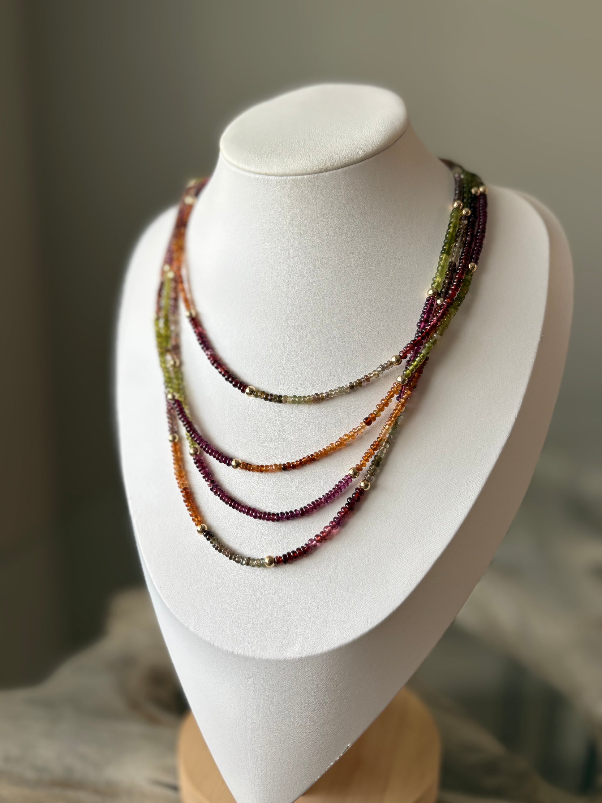 Sapphire Necklace with multiple strands of small, colorful beads and gold accents on a white display bust