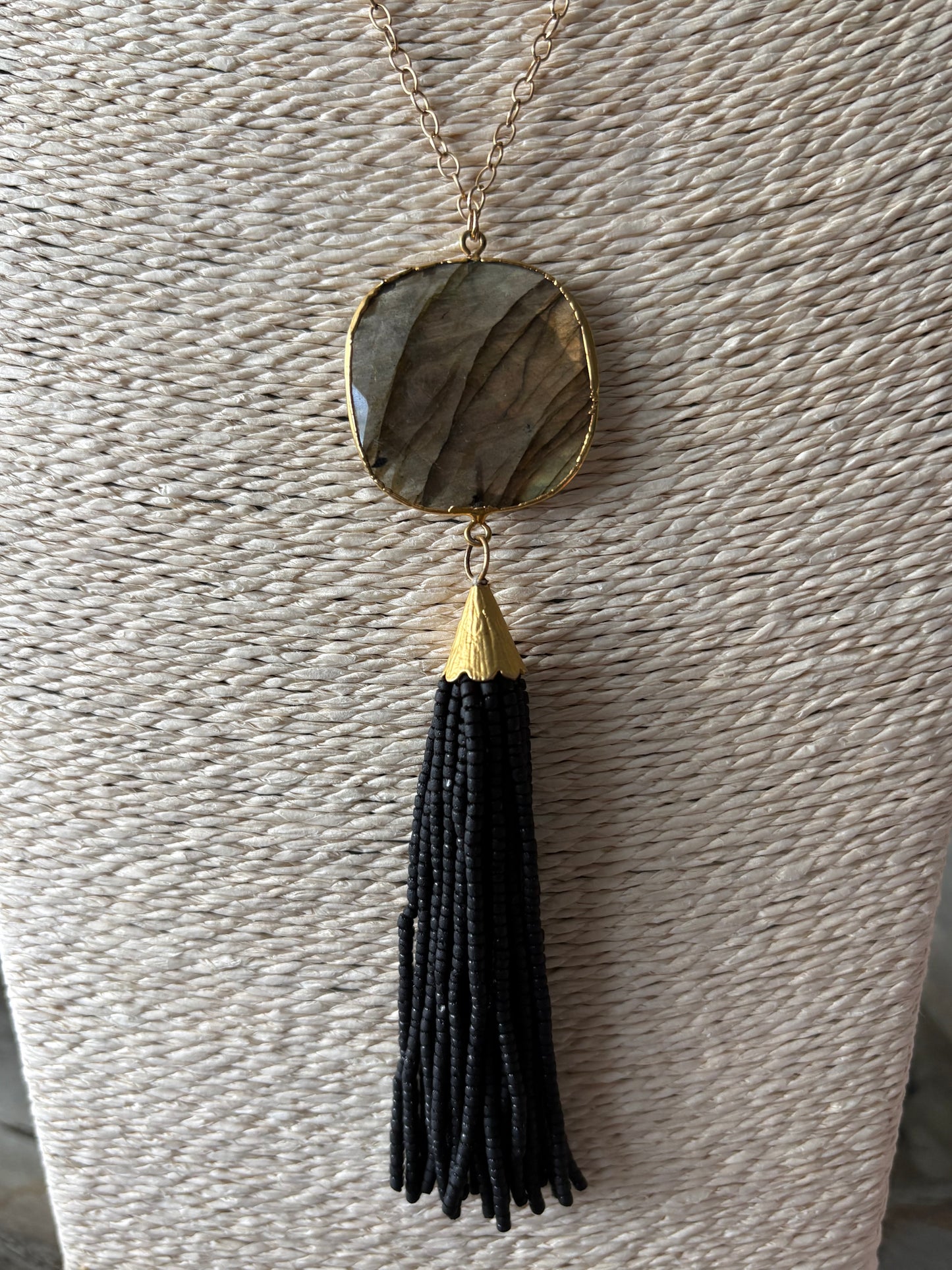 Black Tassel Necklace with a gold chain and a large, flat, oval, grey-brown stone pendant