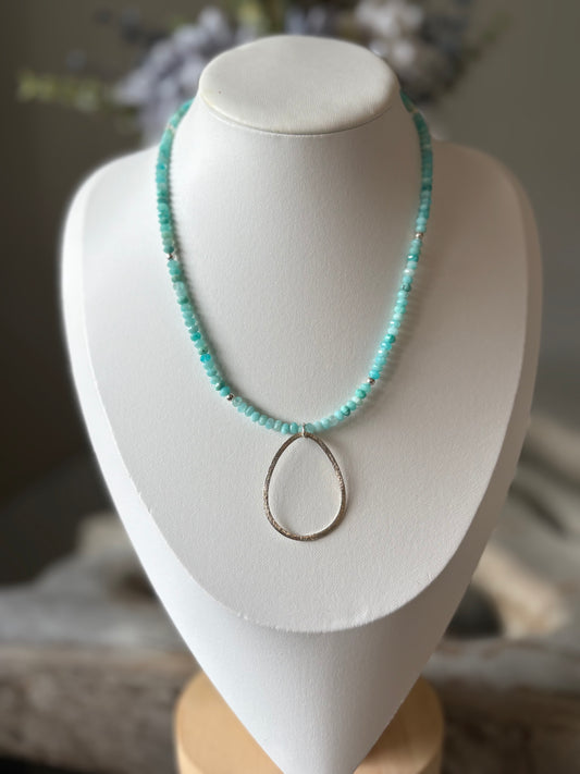 Turquoise beaded necklace with a silver pendant on a white mannequin bust.
