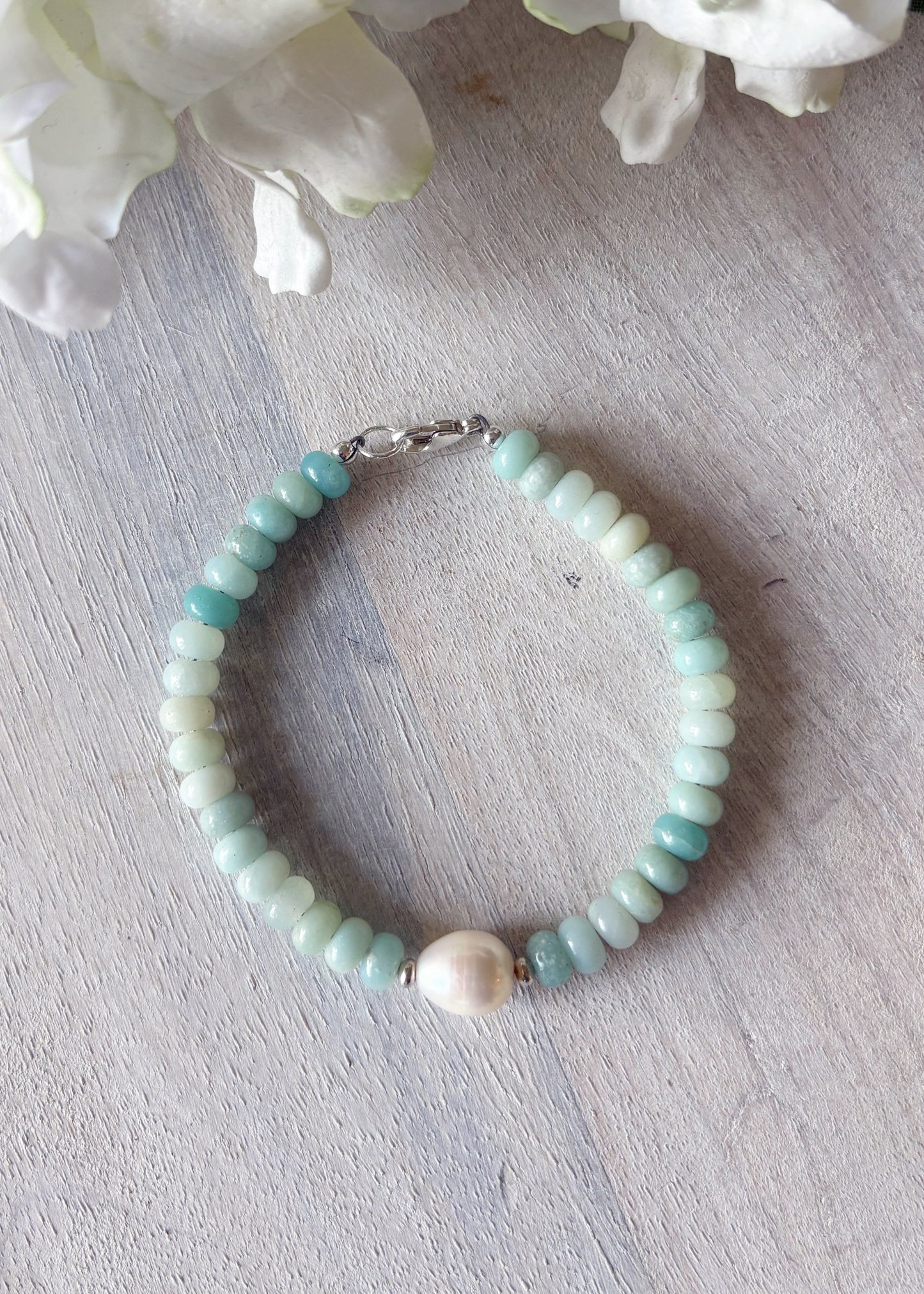 Beaded bracelet with a pink pearl on a light wooden surface with white flowers in the background