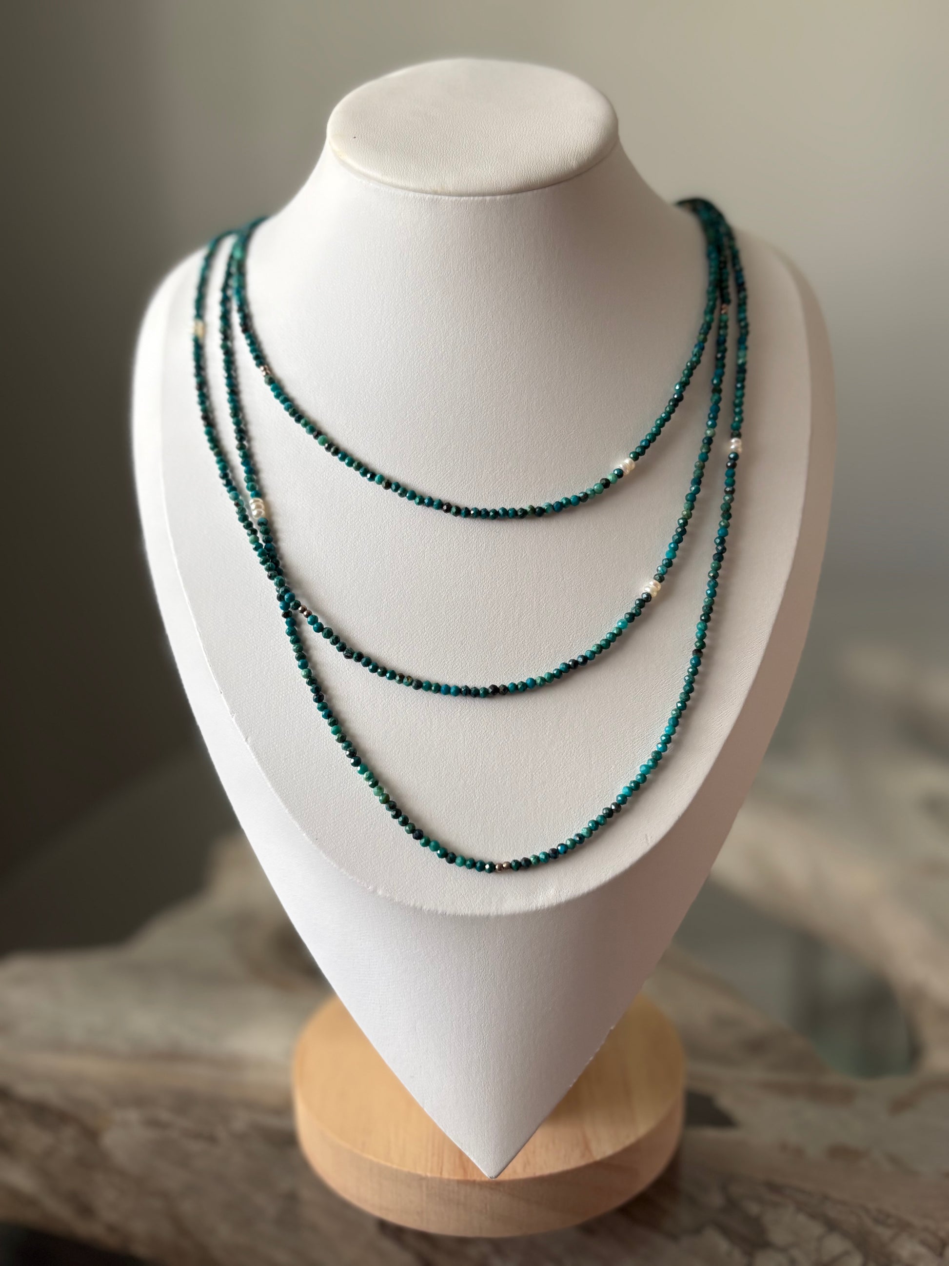 Long Chrysocolla Necklace with three strands of faceted teal beads and white pearls on a white bust