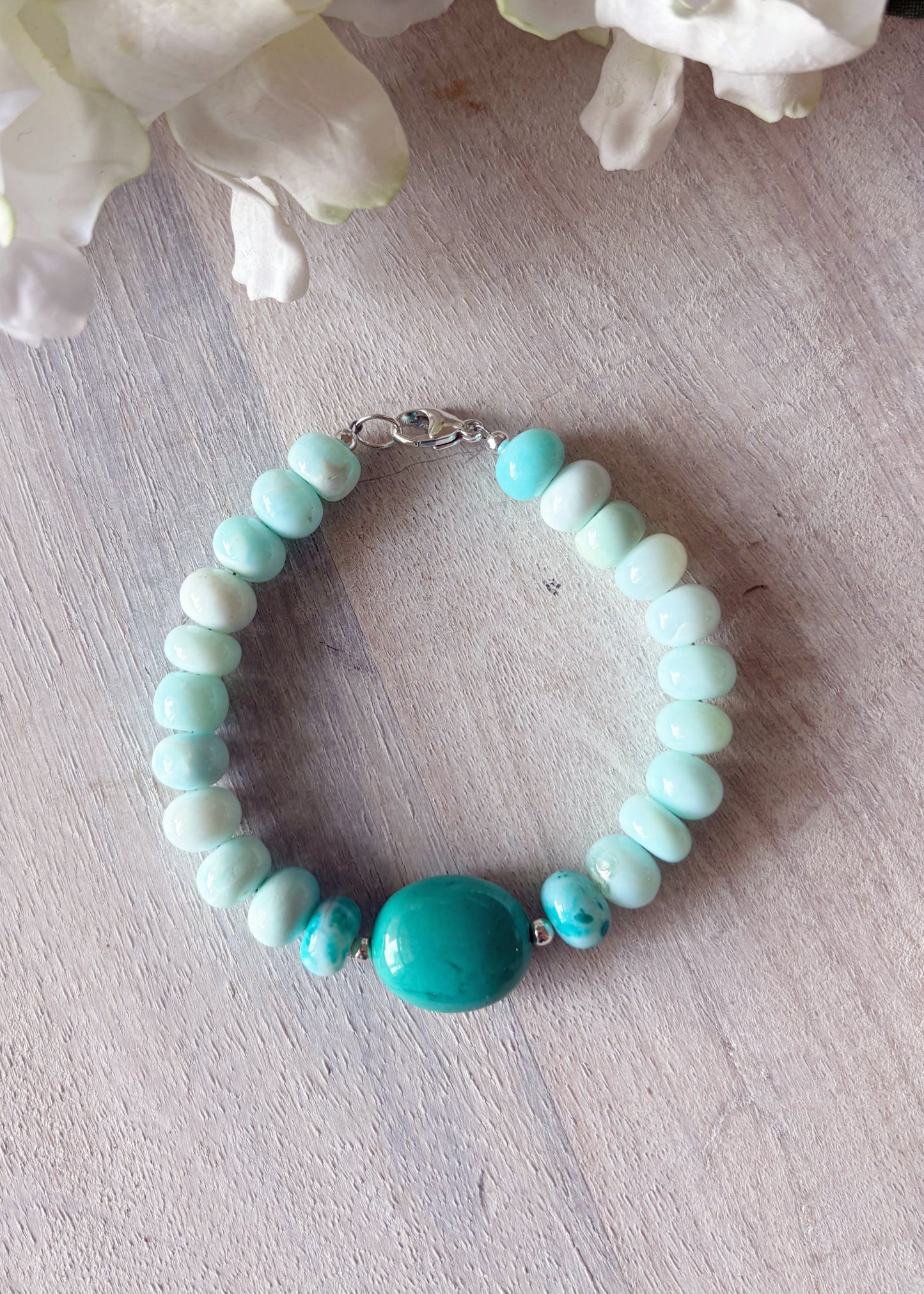 Turquoise beaded bracelet on a light wooden surface with white flowers in the background