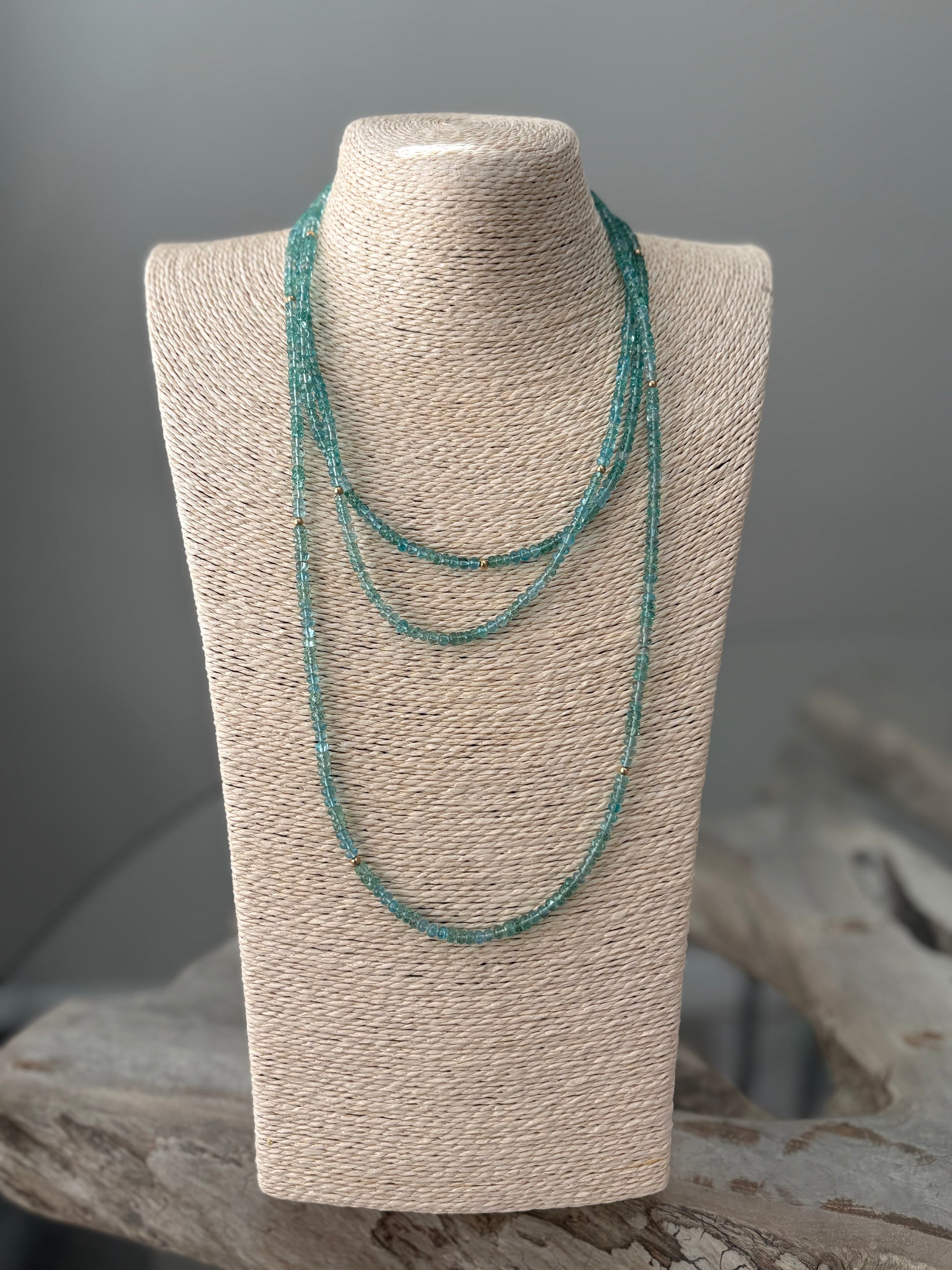 Green beaded necklace on a textured gray stand with a neutral background