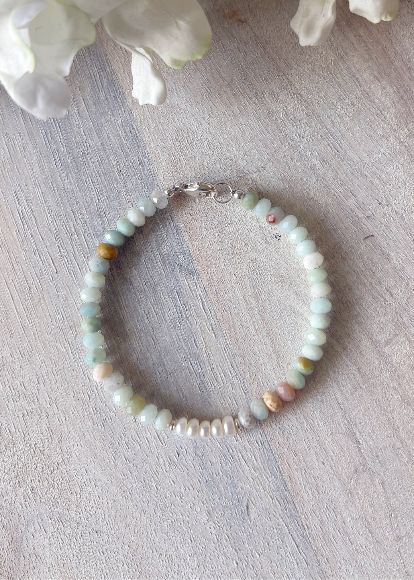 Beaded bracelet on a light wooden surface with white flowers in the background
