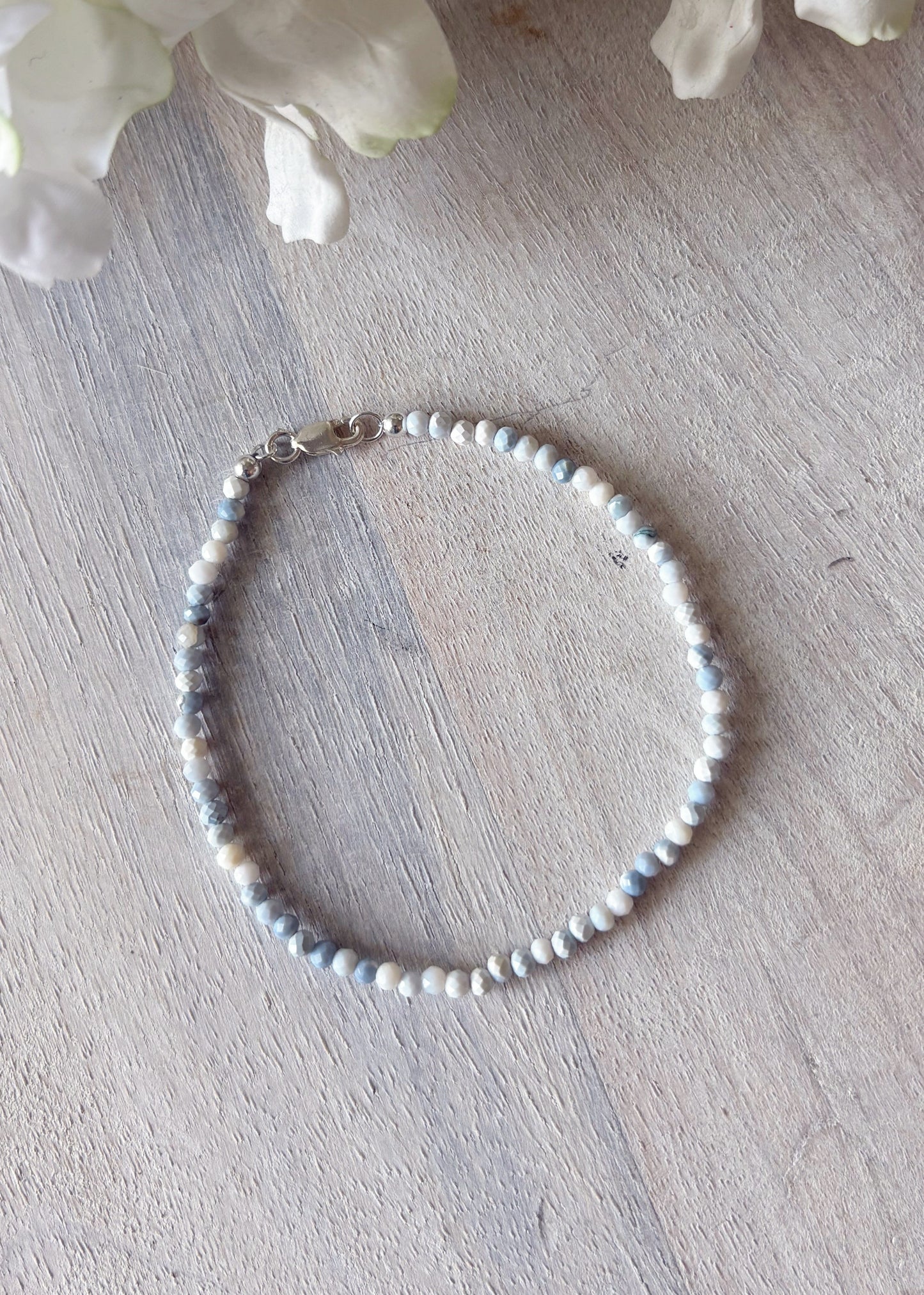 Pearl bracelet on a wooden surface with white flowers in the background