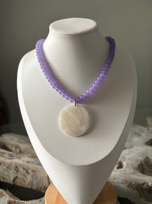 A beaded necklace with light purple beads and a round iridescent white shell pendant, displayed on a white jewelry bust.