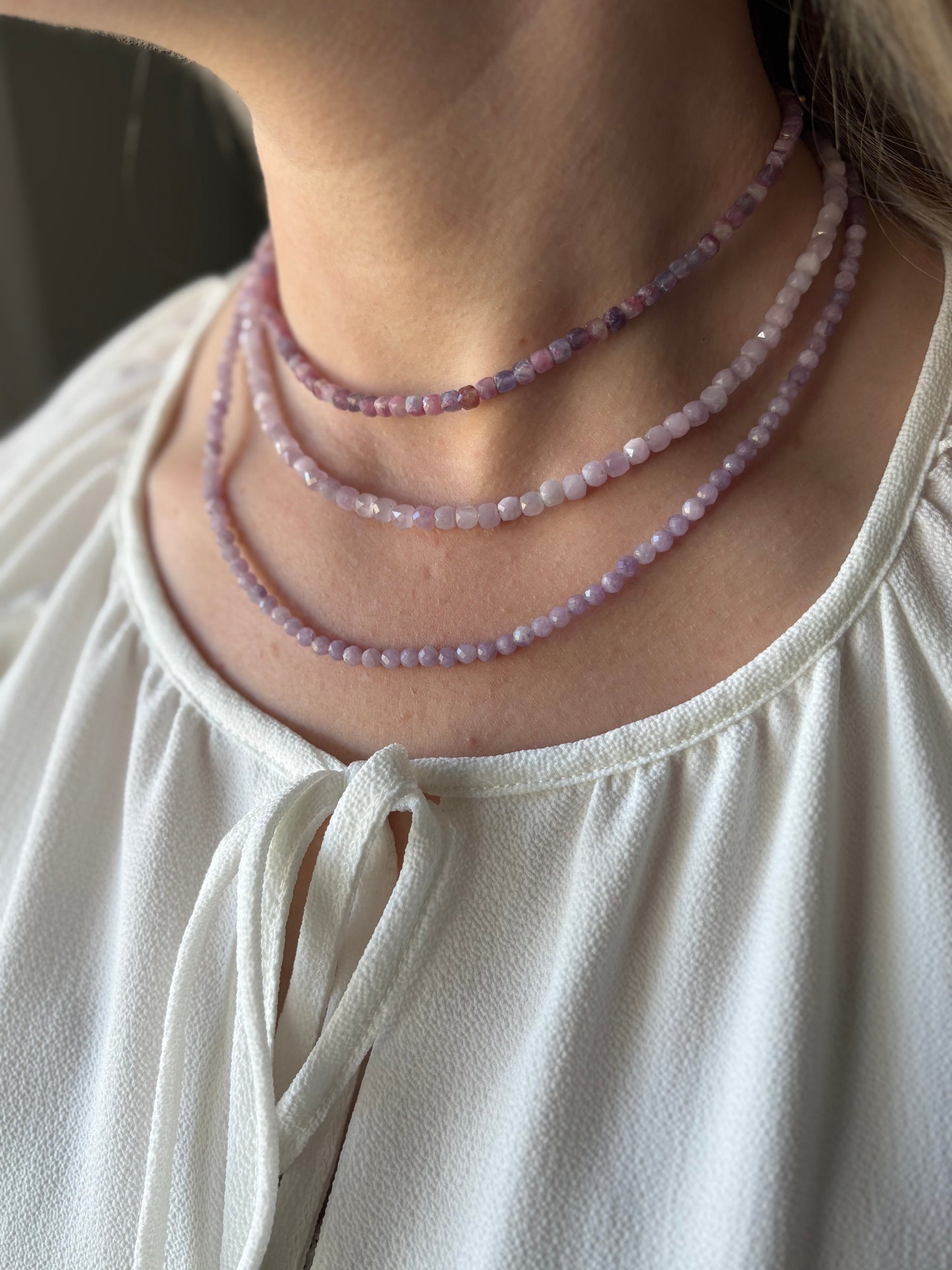 Kunzite Cube Necklace with three strands of light purple beads on a person's neck