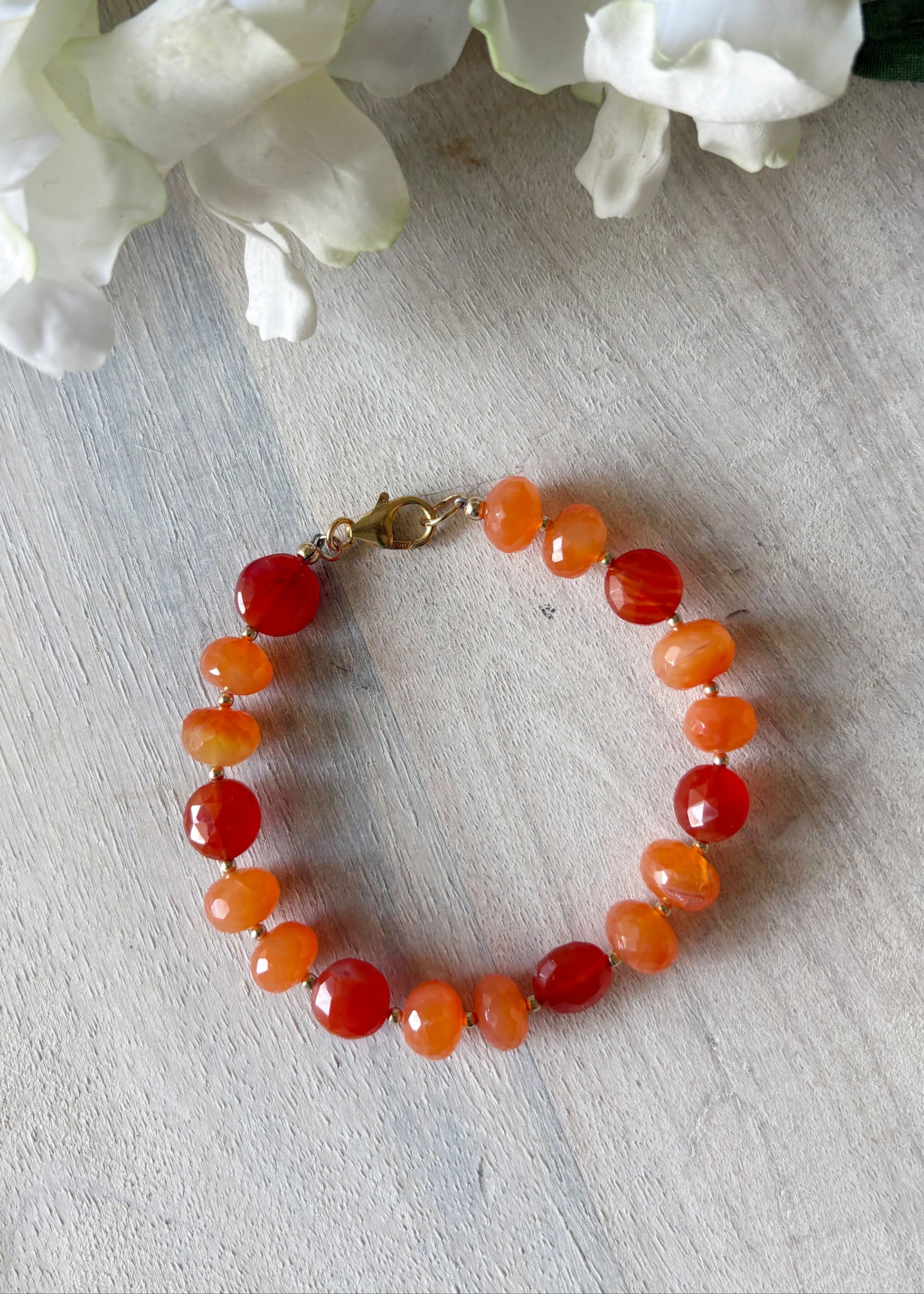 Bracelet with orange beads on a light wooden surface with white flowers in the background