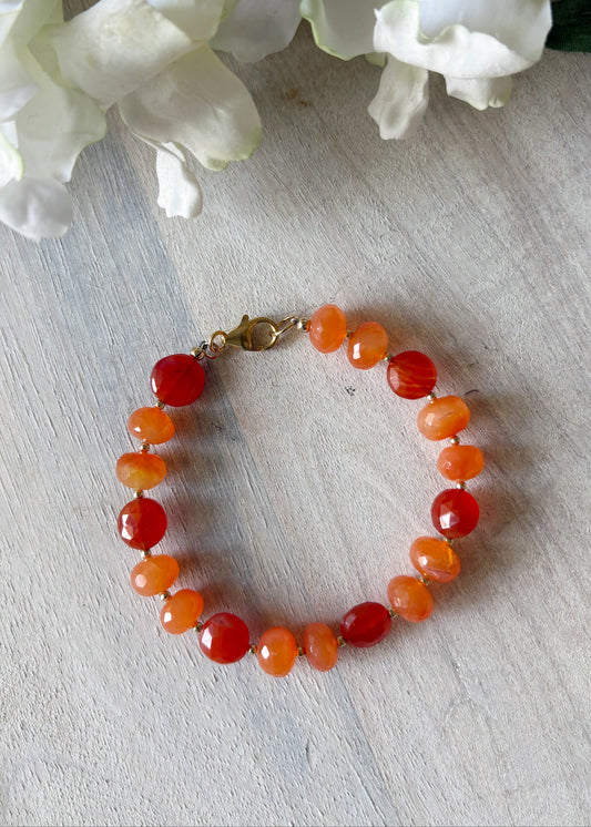 Bracelet with orange beads on a light wooden surface with white flowers in the background