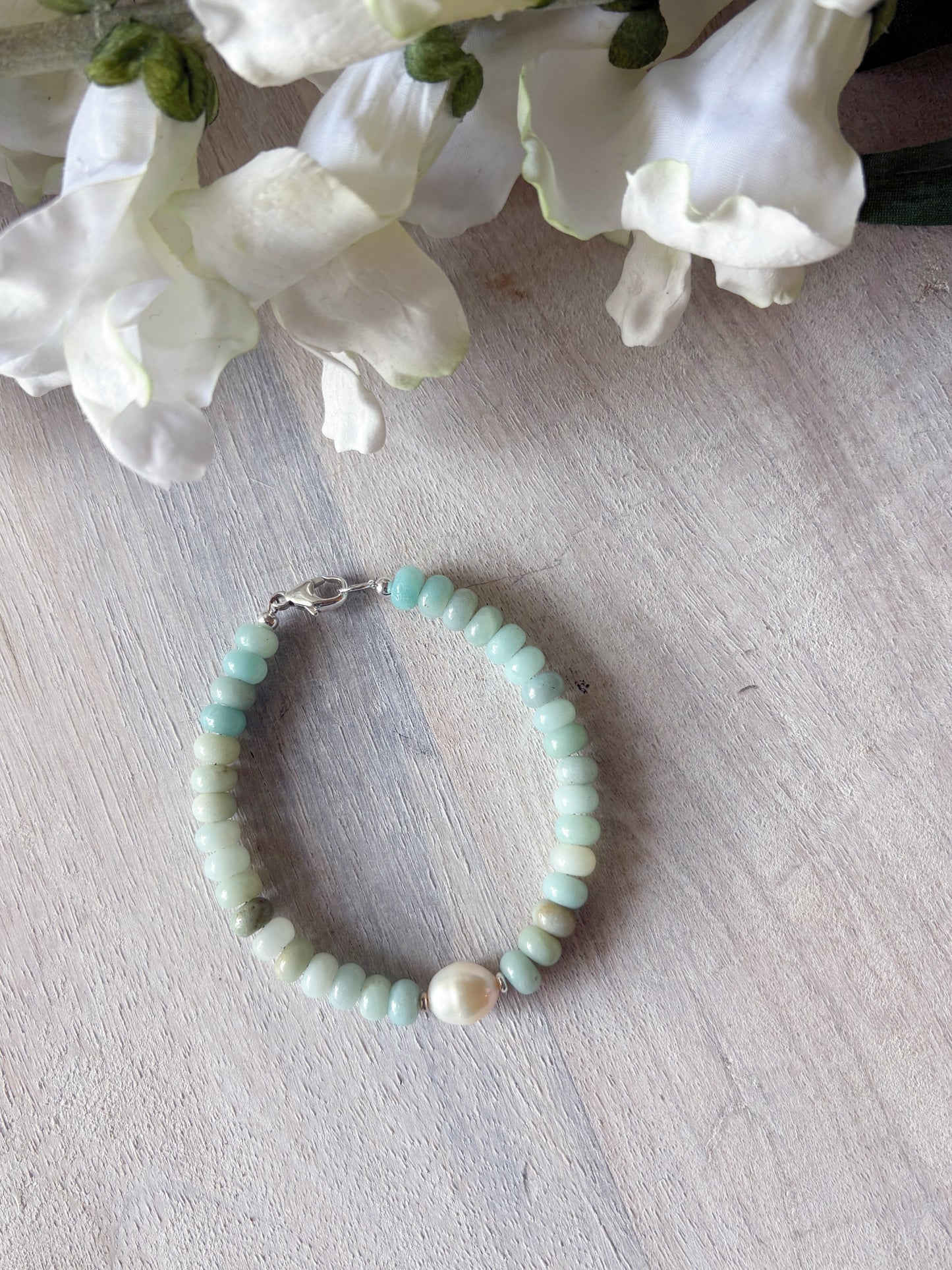 Beaded bracelet with a pearl on a light wooden surface with white flowers in the background
