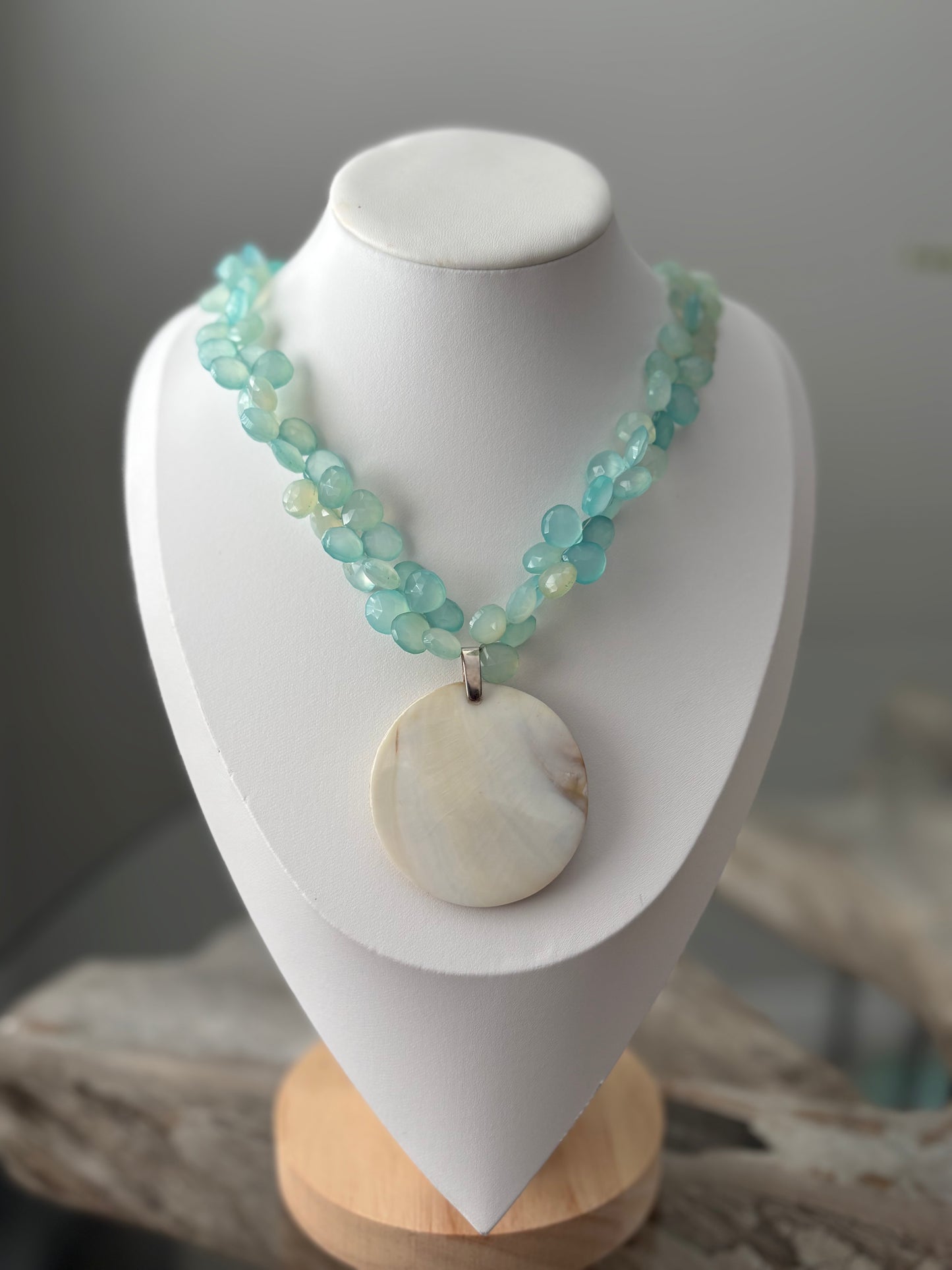 Necklace with turquoise beads and a large shell pendant on a white mannequin bust.