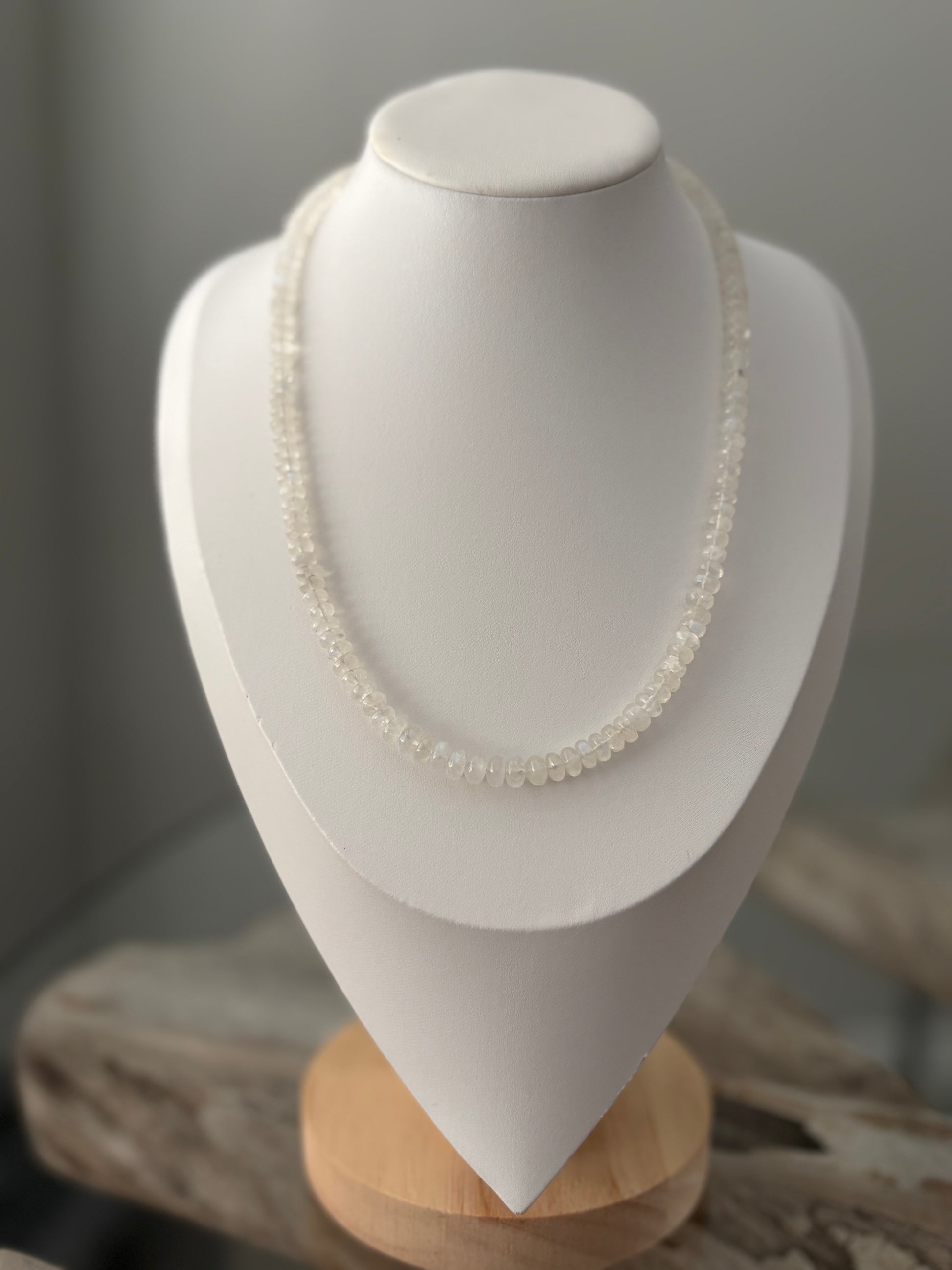 Pearl necklace on a white mannequin bust with a wooden base against a neutral background