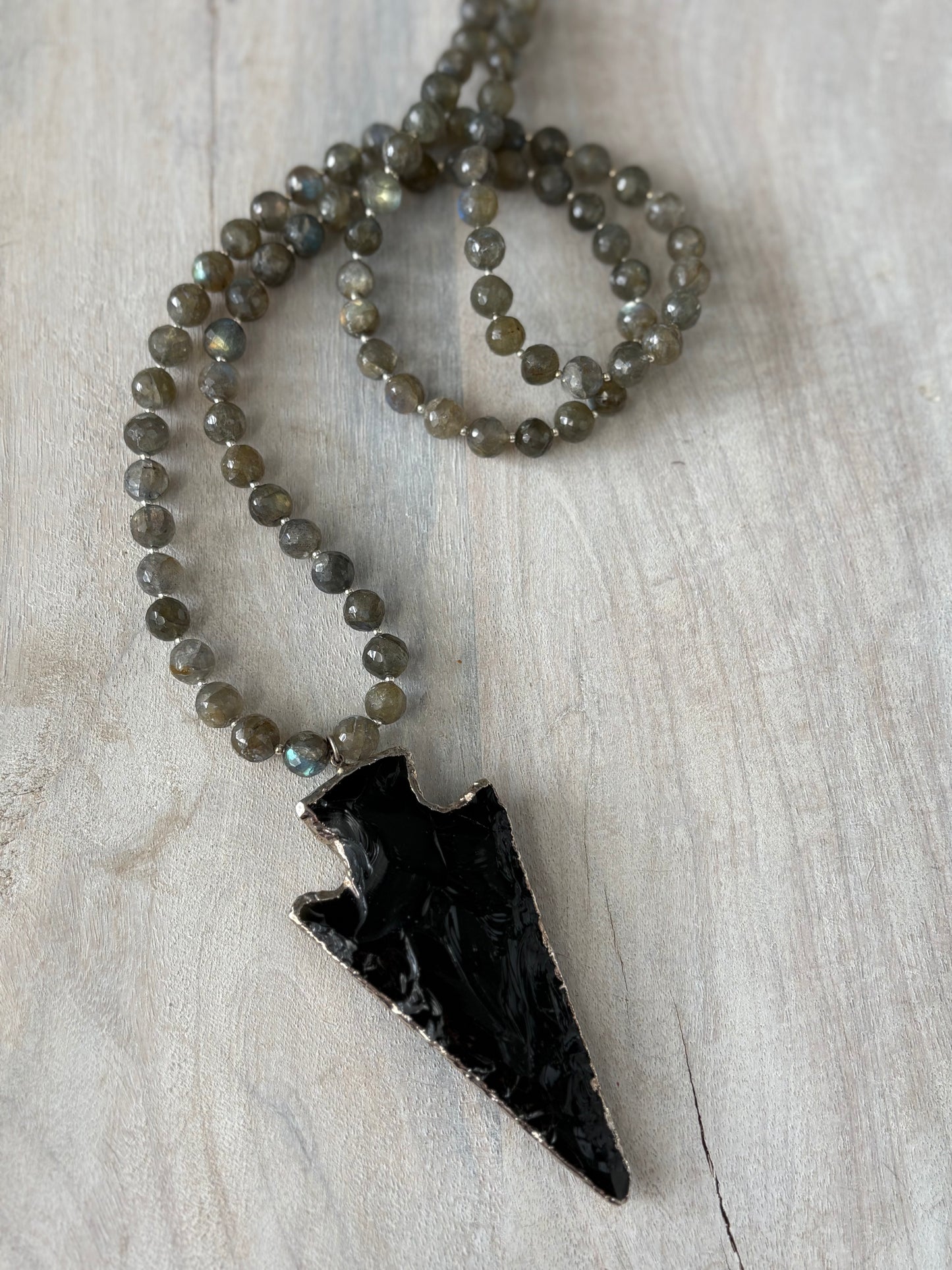 Necklace with black arrowhead pendant and beaded chain on a light wooden surface