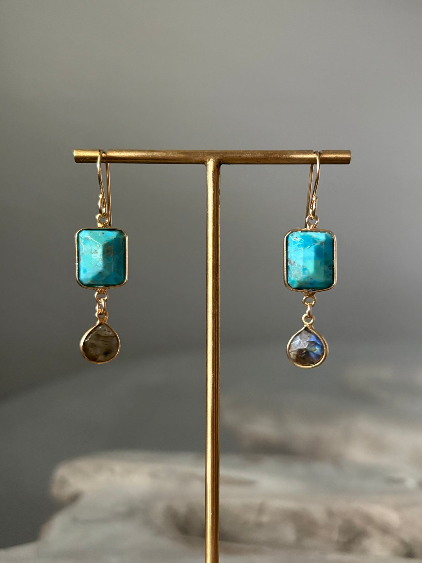 Pair of earrings with turquoise stones on a gold stand against a gray background