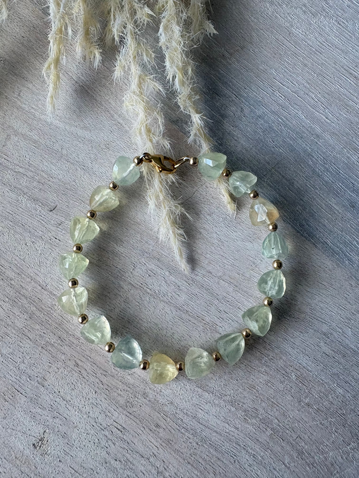 Green beaded bracelet on a textured surface with dried plants