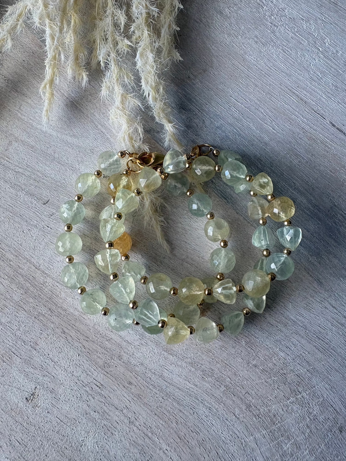 Green beaded bracelet on a textured surface with a plant leaf