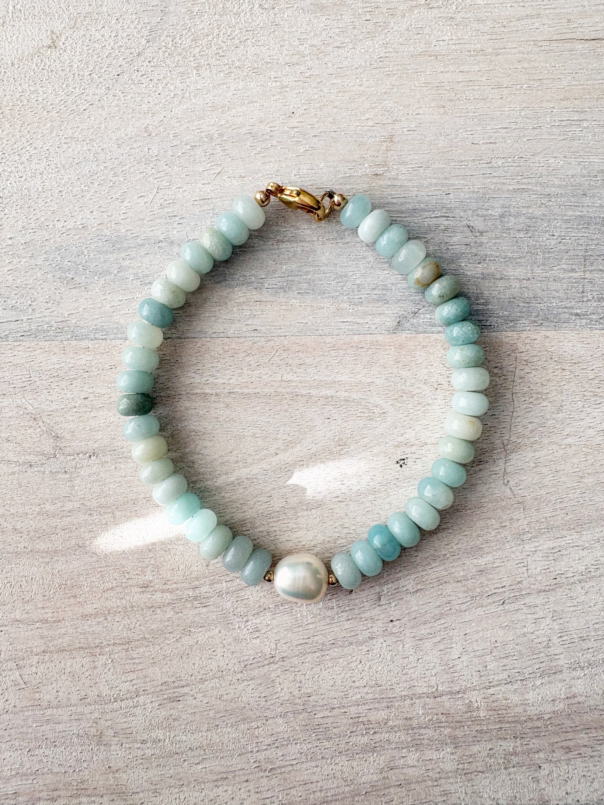 Amazonite and Pearl Bracelet with light blue beads and a single white pearl on a light wooden surface