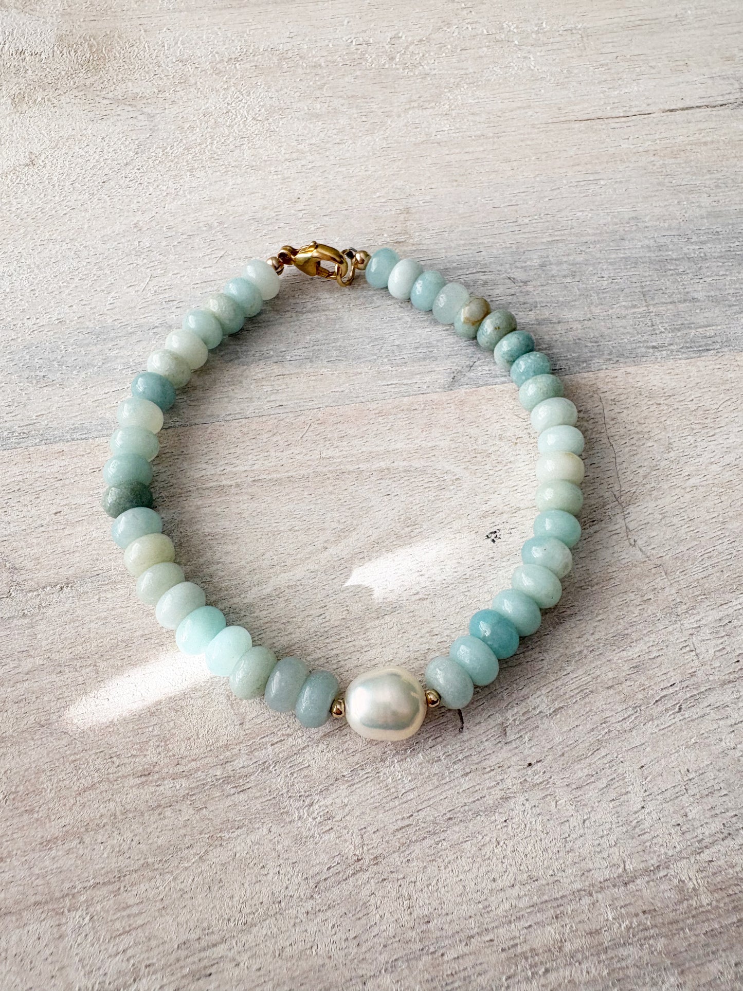 Amazonite and Pearl Bracelet with light blue beads and a single white pearl on a light wooden surface