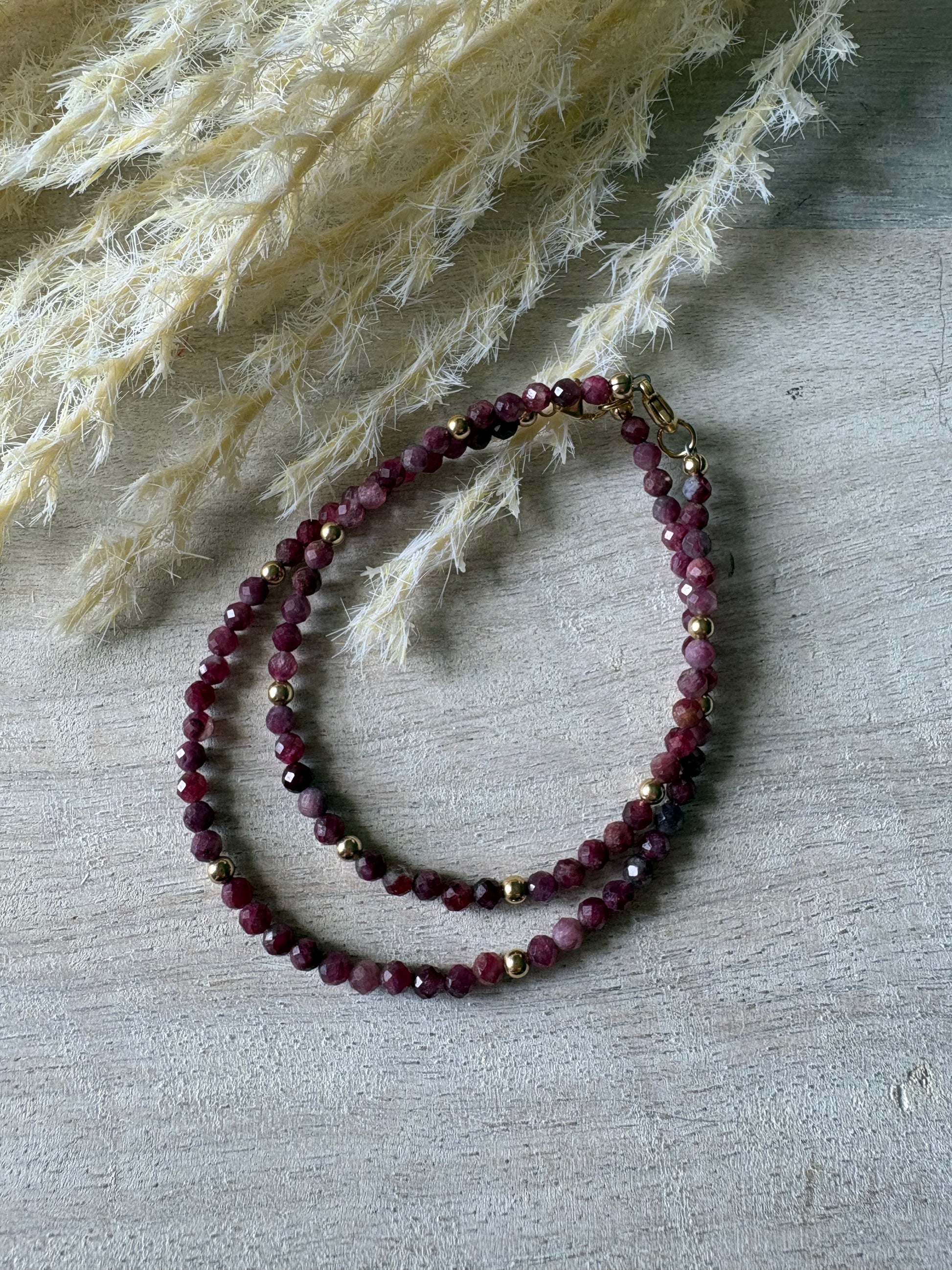 Pink Tourmaline Bracelet with faceted beads and gold accents on a light wooden surface with dried grass