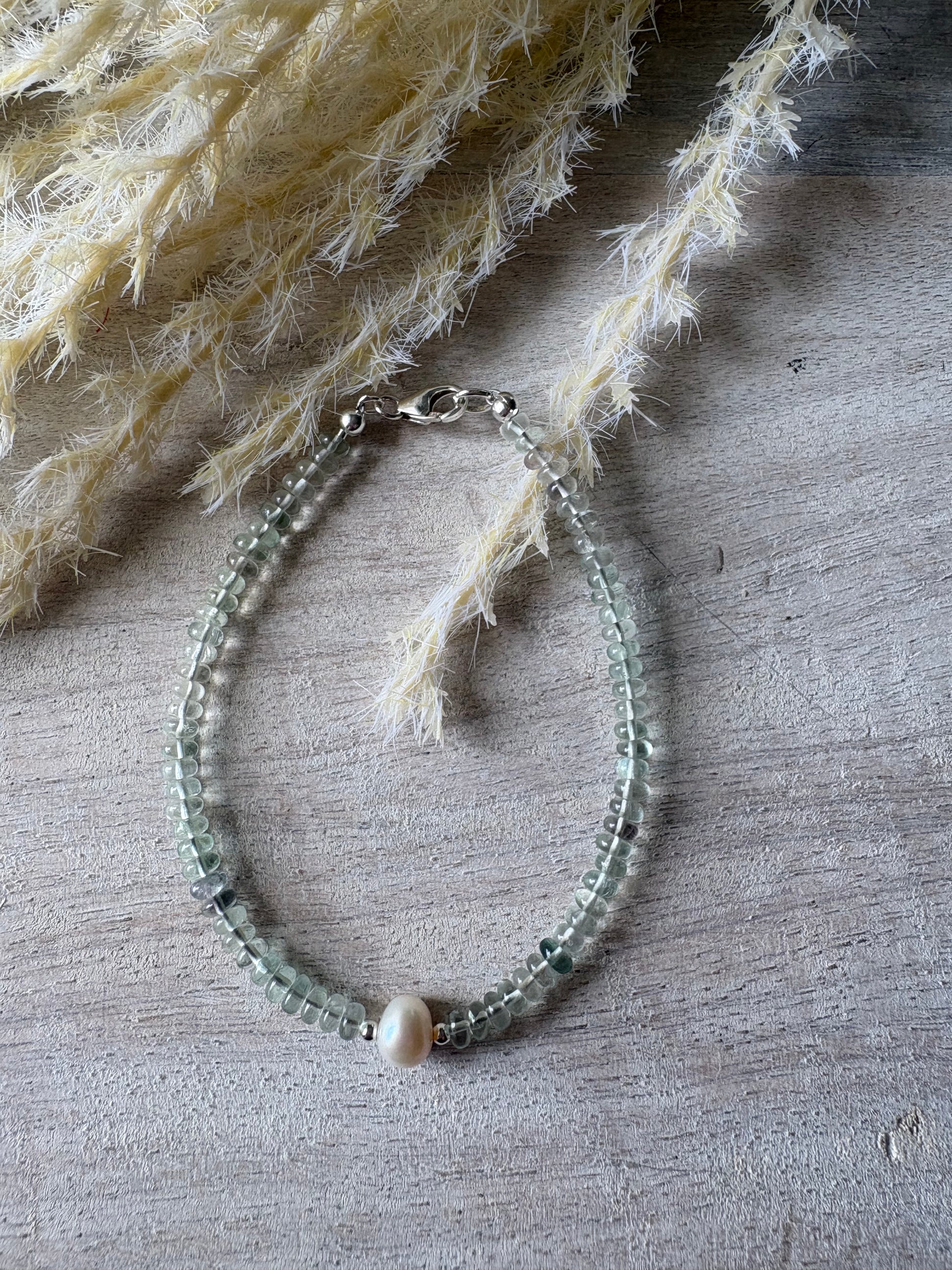 Fluorite and Pearl Bracelet with light green beads and a single white pearl on a wooden surface