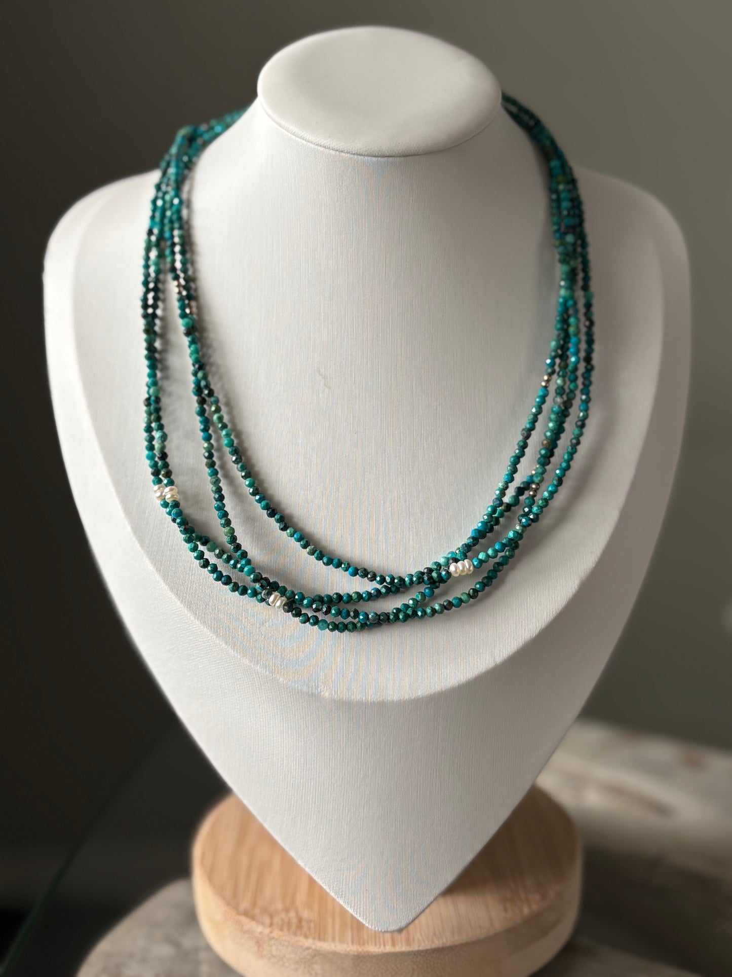 Long Chrysocolla Necklace with three strands of faceted teal beads and white pearls on a white bust