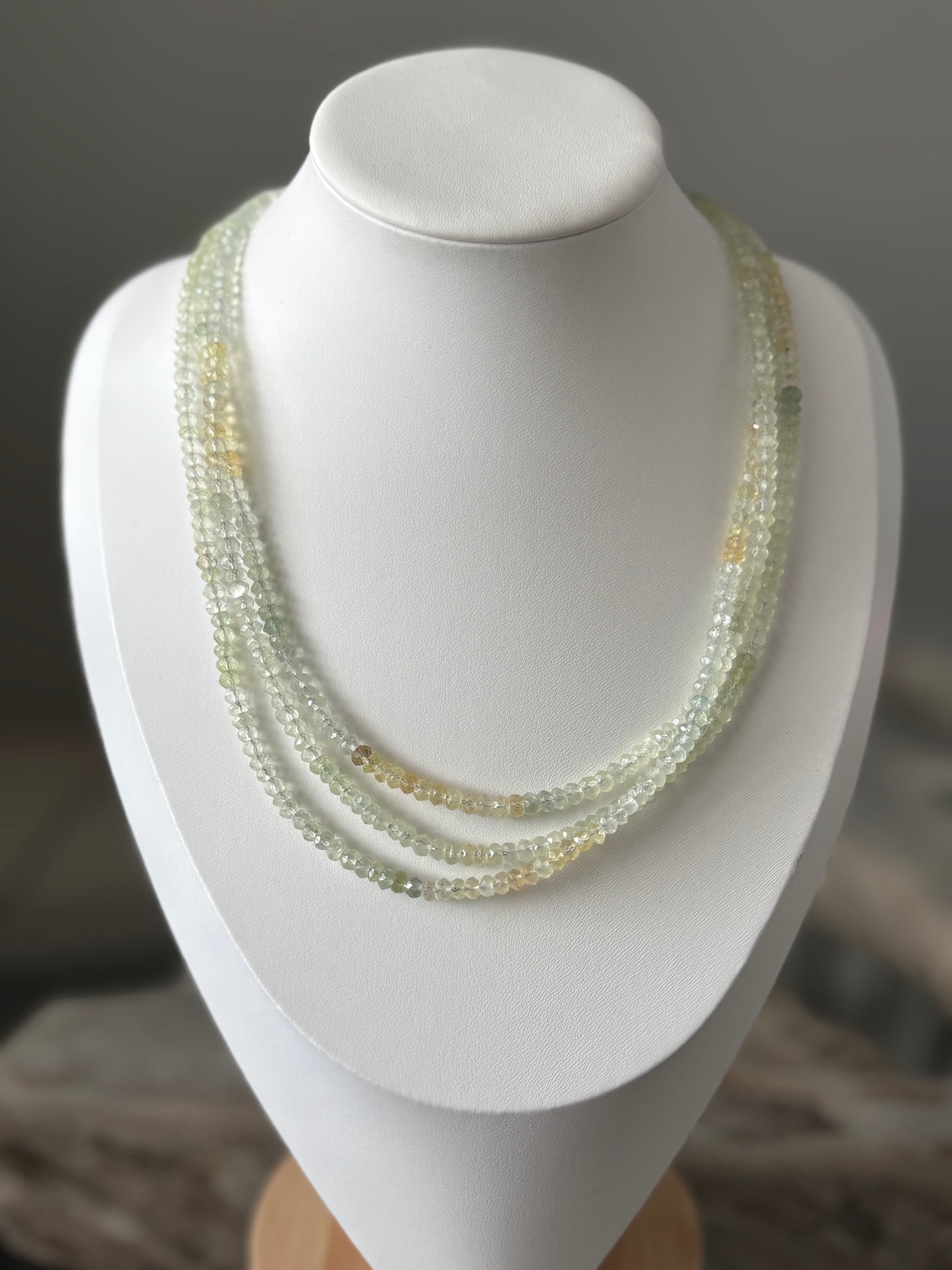 Long Prehnite Necklace with three strands of faceted light green and yellow beads on a white bust